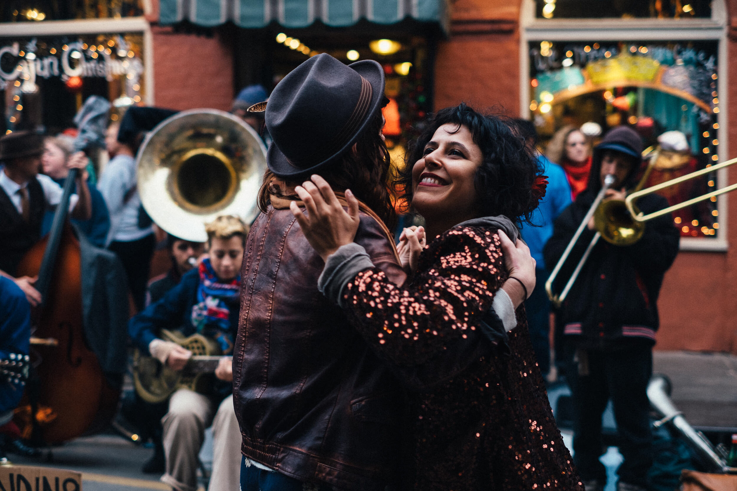 Two women dancing closely together at a lively outdoor event with musicians playing instruments in the background.