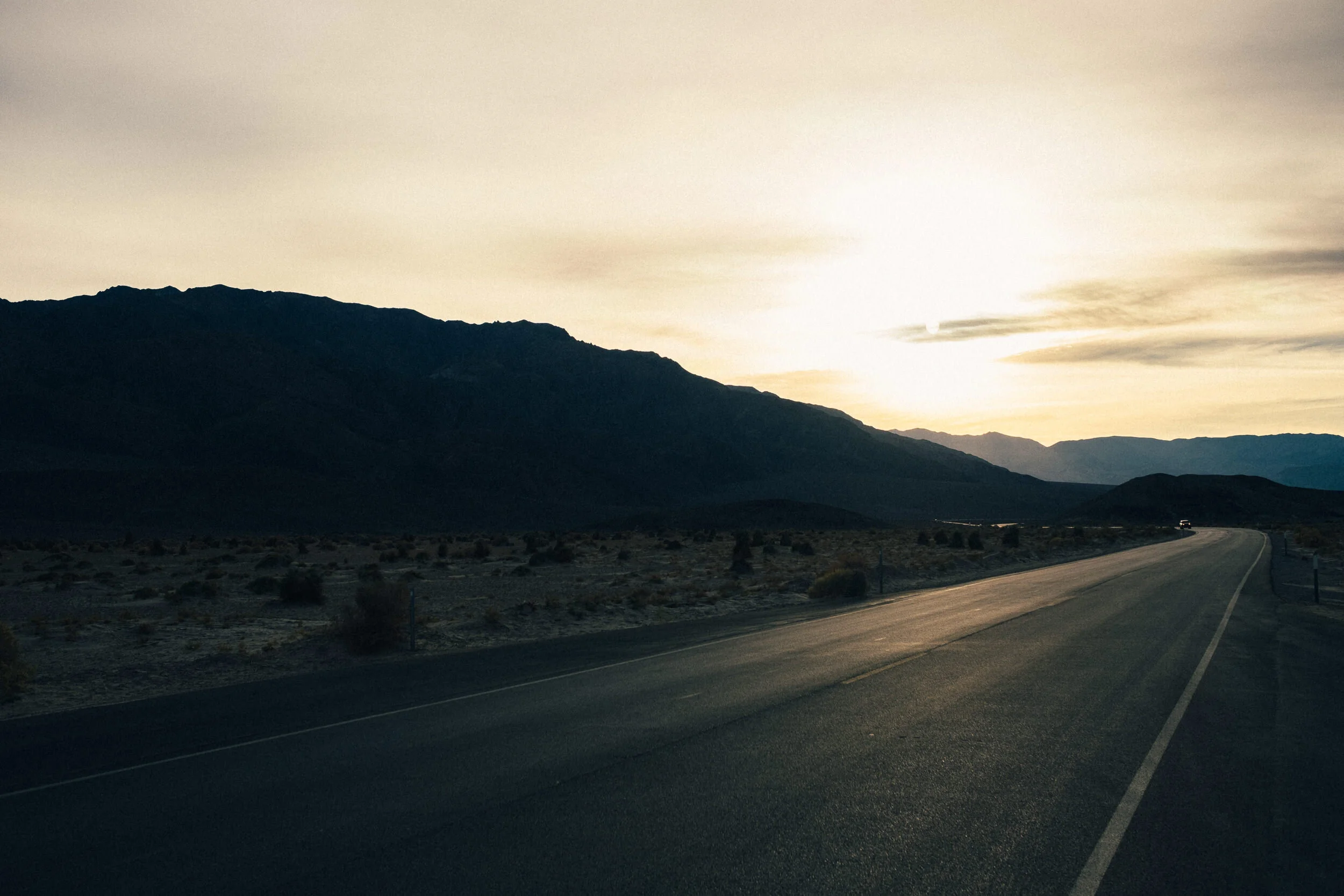 Scenic view of a desert landscape with mountains and a sky at sunset, a winding road in the foreground.