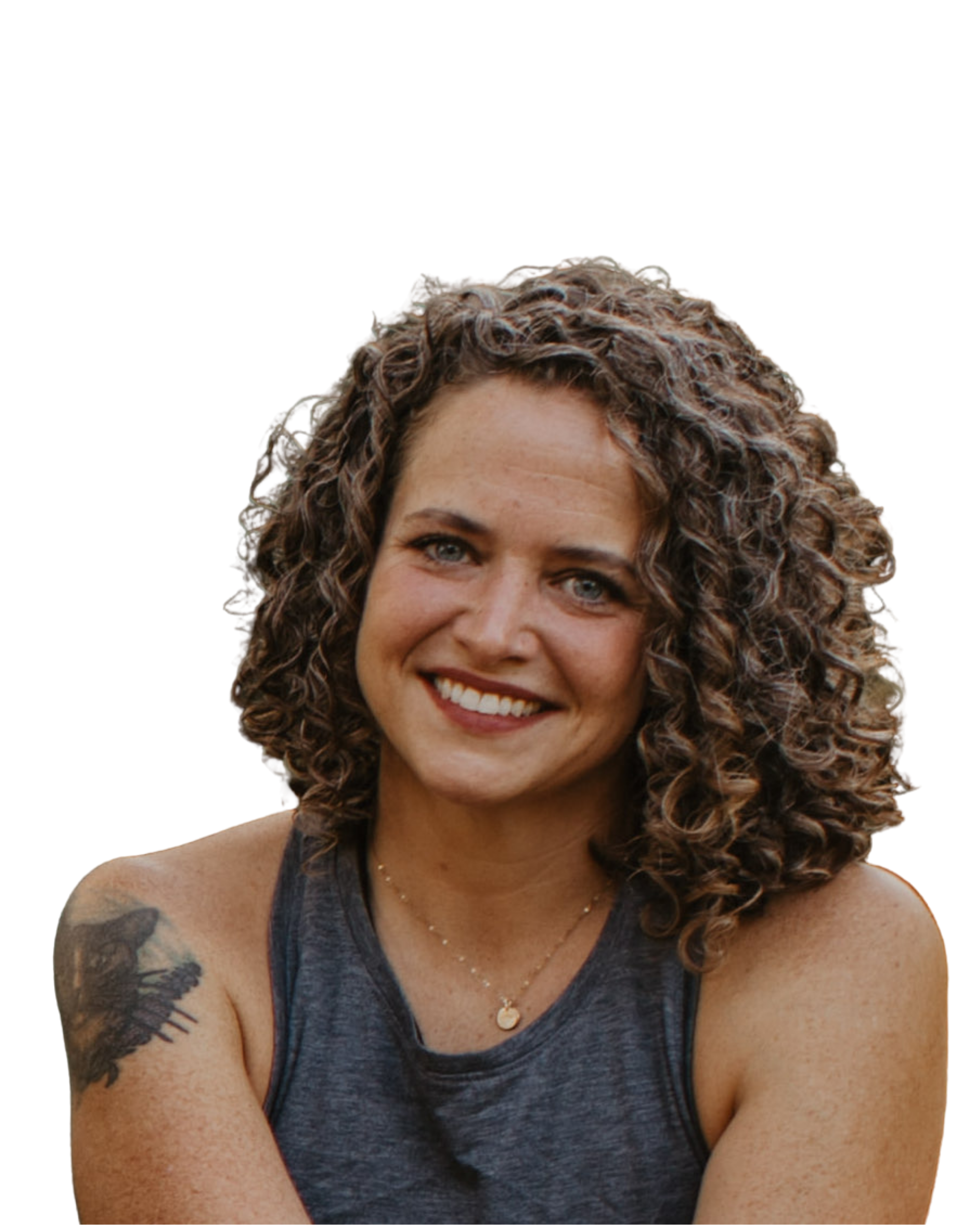 A woman with curly hair smiling, wearing a dark sleeveless top and a necklace, with a tattoo on her upper arm.