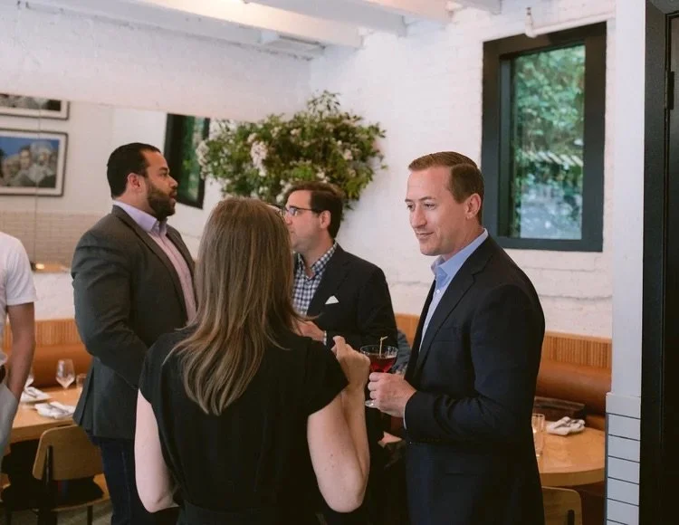 People socializing indoors at a restaurant or event, with men in suits and a woman with long hair.