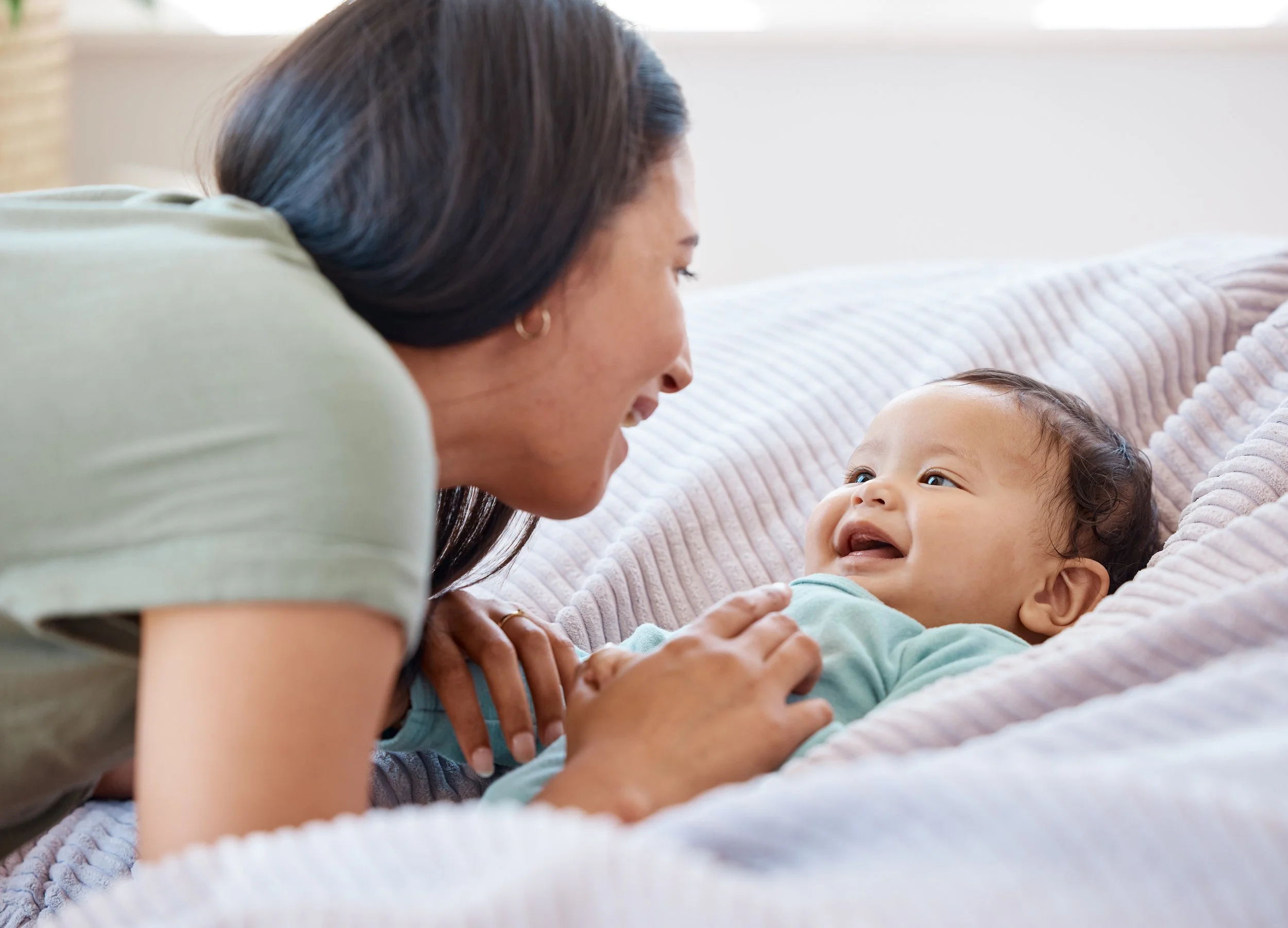 An older woman and a young child lying on their sides on a bed, facing each other, smiling and looking into each other's eyes.