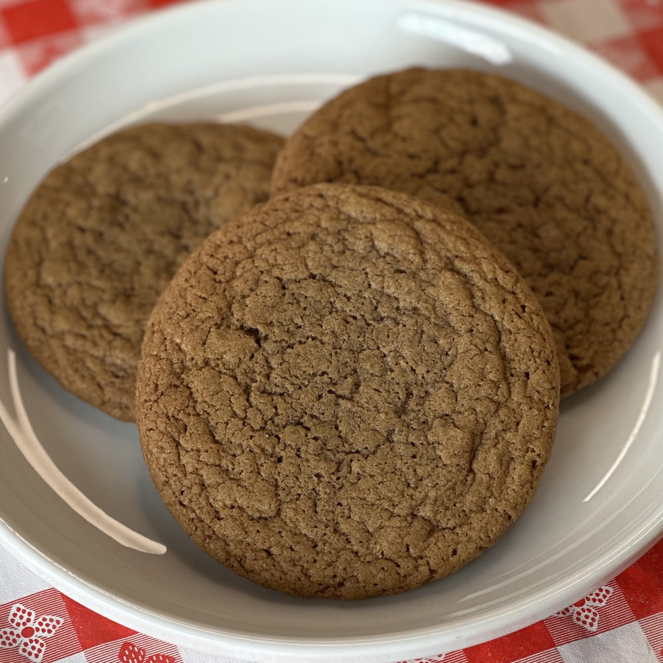 Close-up of three chocolate cookies in a white bowl on a red and white checkered tablecloth.