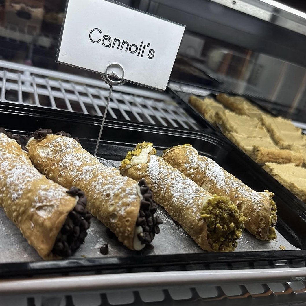 Cannoli pastry desserts with chocolate chips and pistachio toppings displayed in a bakery case.