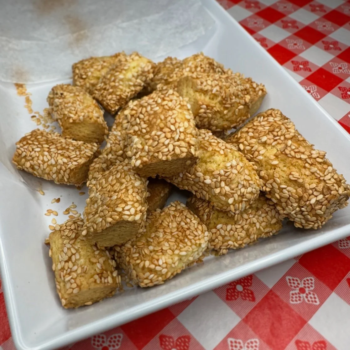 Sesame-topped tofu bites served on a white plate, with a red and white checkered tablecloth underneath.