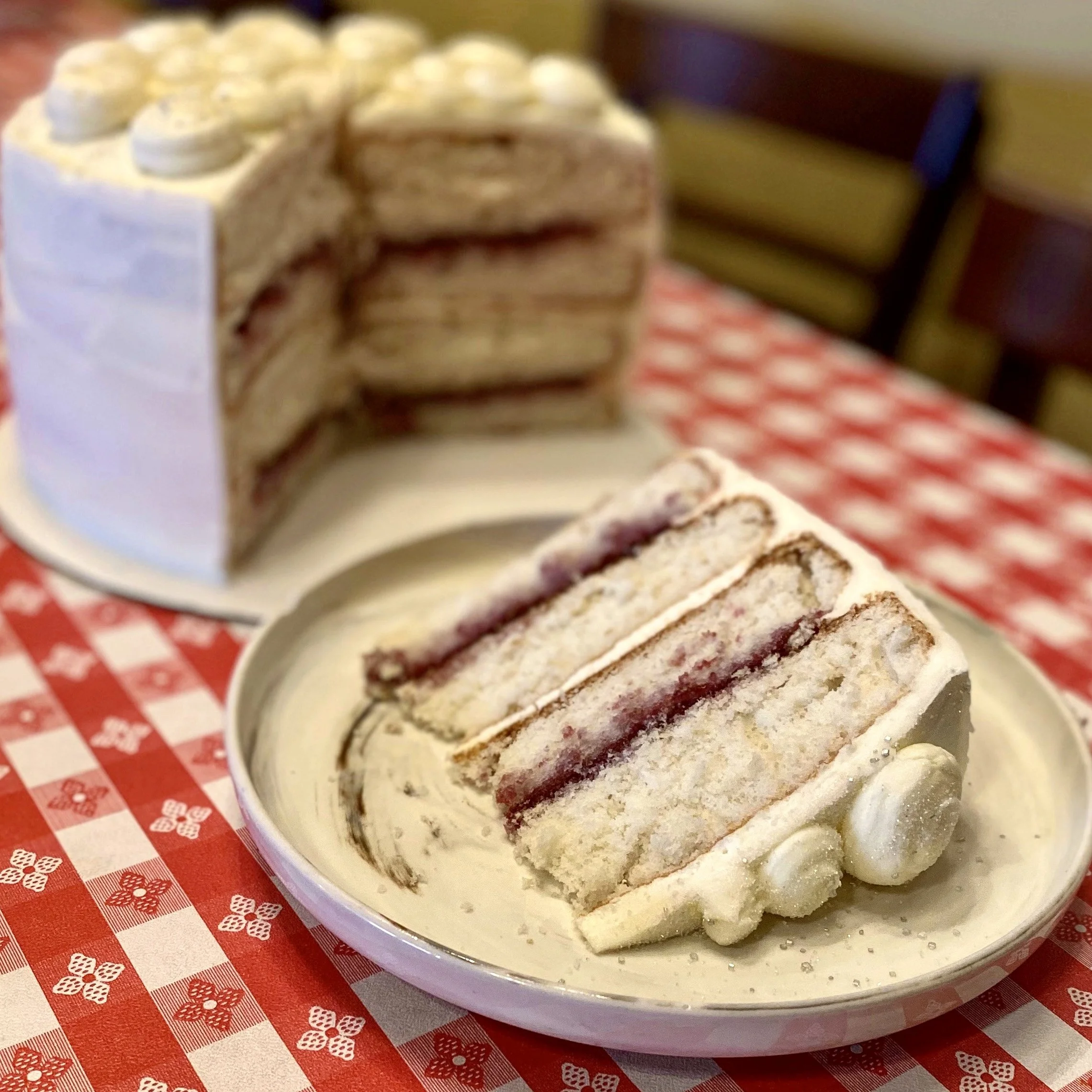 A bowl of ice cream with cookie layers, topped with white frosting and small white decorations, placed on a red and white checkered tablecloth.