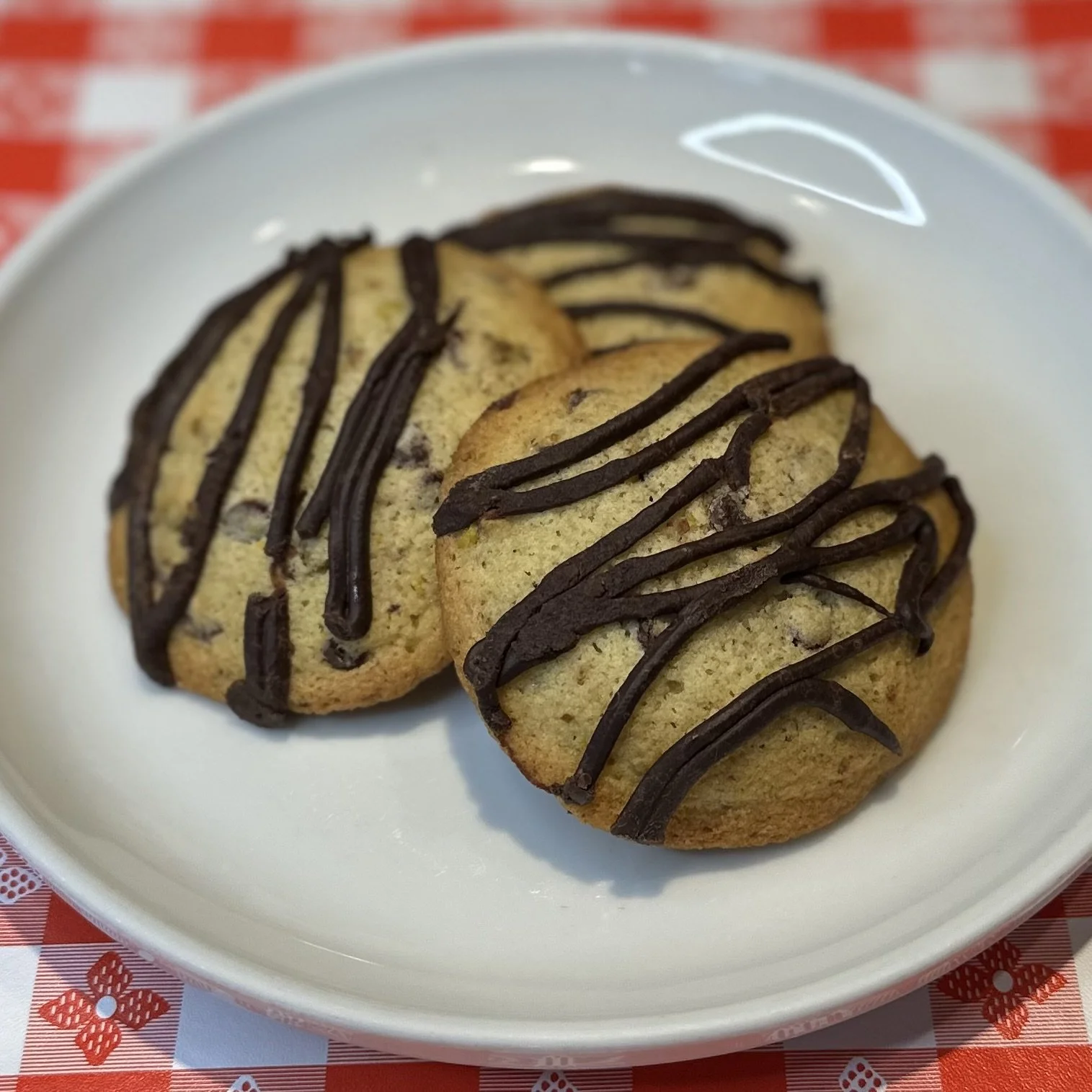Chocolate chip cookies drizzled with chocolate on a white plate.