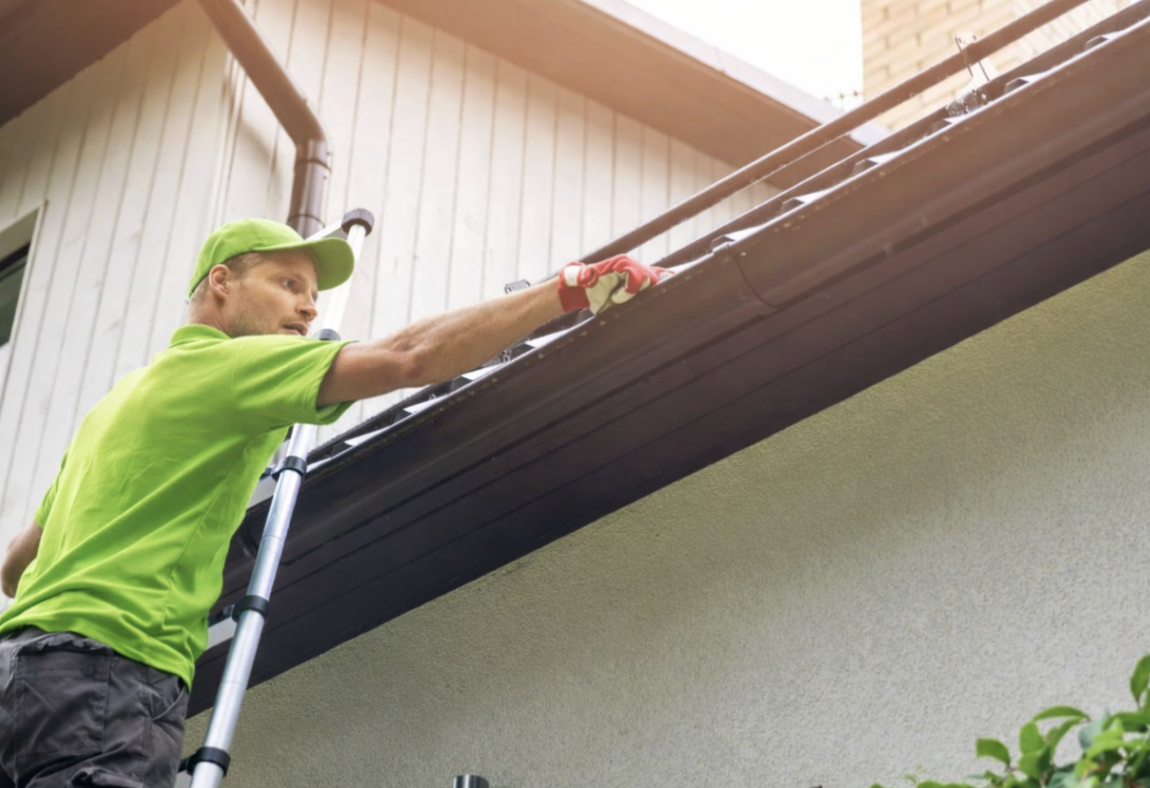 Man on a ladder installing or repairing a gutter on the side of a house.