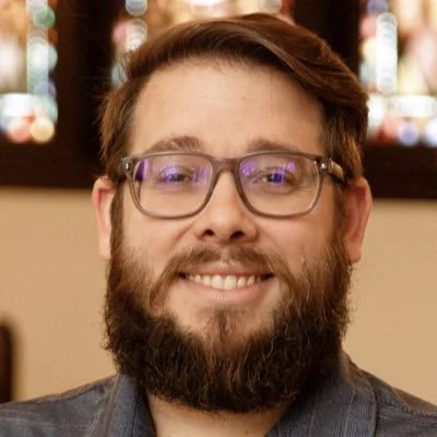 Portrait of a man with glasses and a beard, smiling indoors.