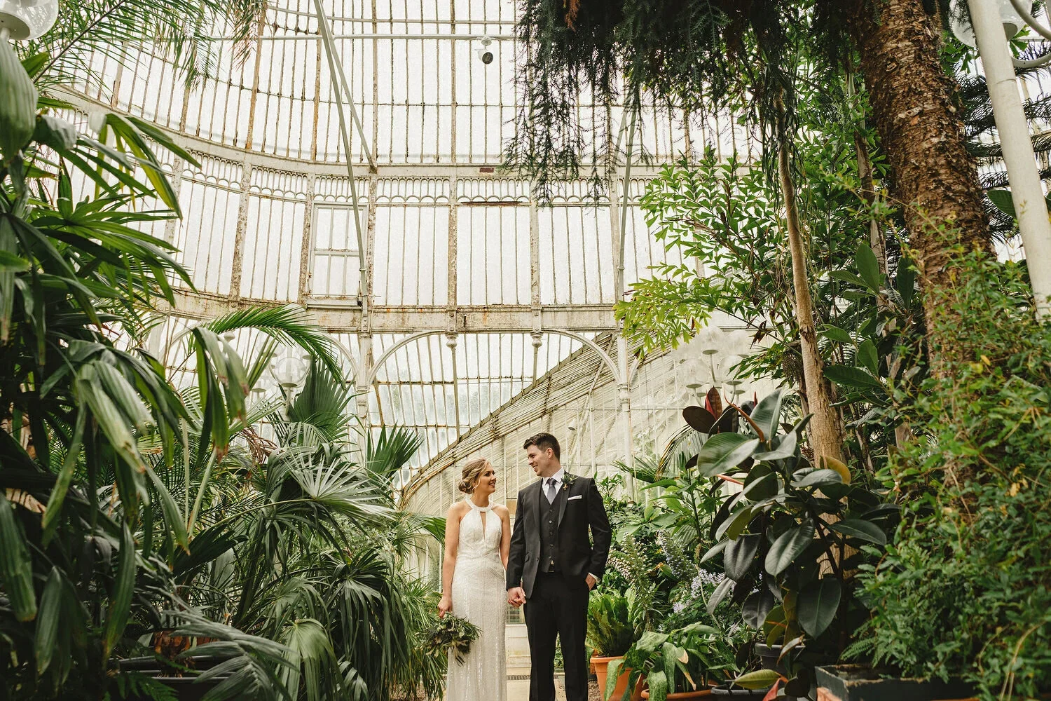 A bride and groom holding hands in the Palm house in Belfast Botanic Gardens