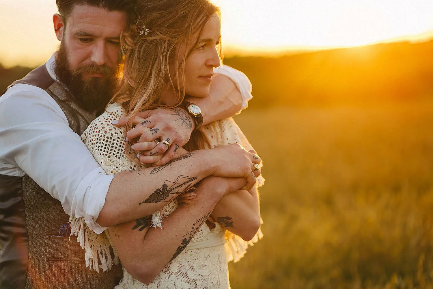 A bearded groom and his wife with tattoos in an embrace during sunset in a field during their elopement in Northern Ireland.