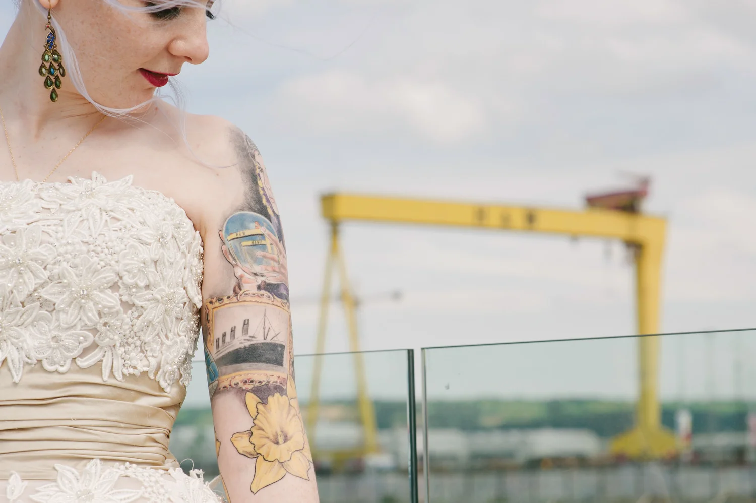 A bride with tattoos posed in front of the Harland and Wolf Cranes