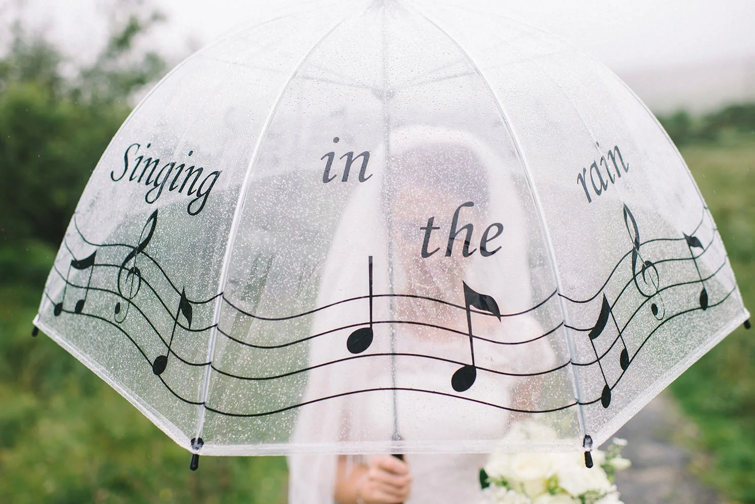 A bride holding a wedding umbrella that says singing in the rain