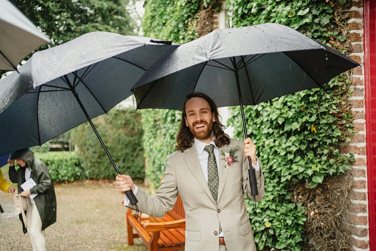 An usher at a rainy wedding in Northern Ireland holding two umbrellas