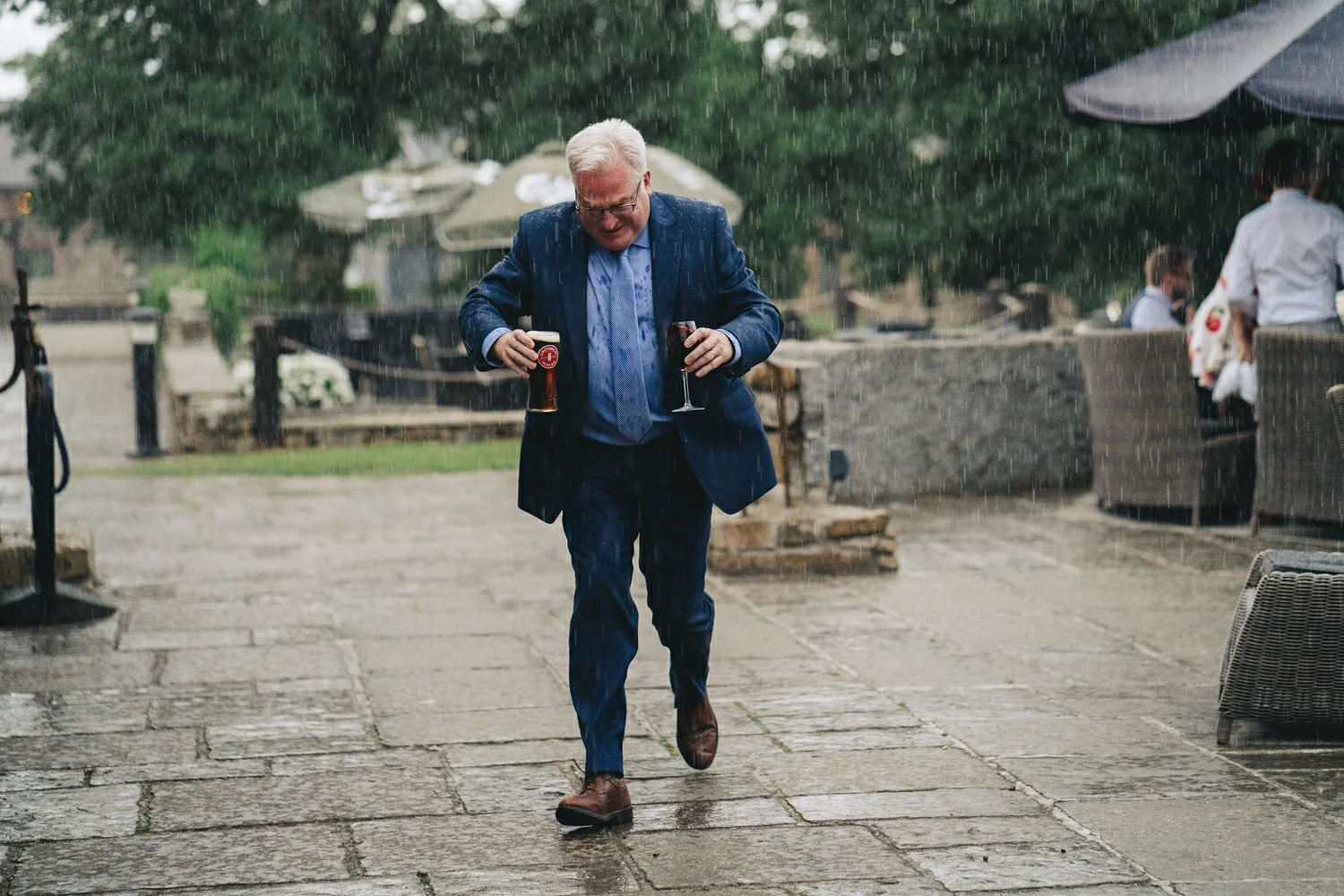 A wedding guest holding two drinks running to get out of the rain