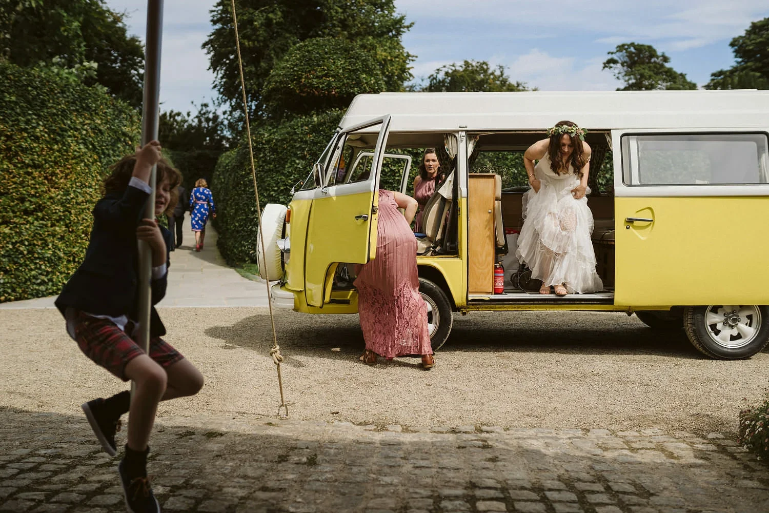 A bride getting out of a vintage VW camper while her son plays in the foreground.