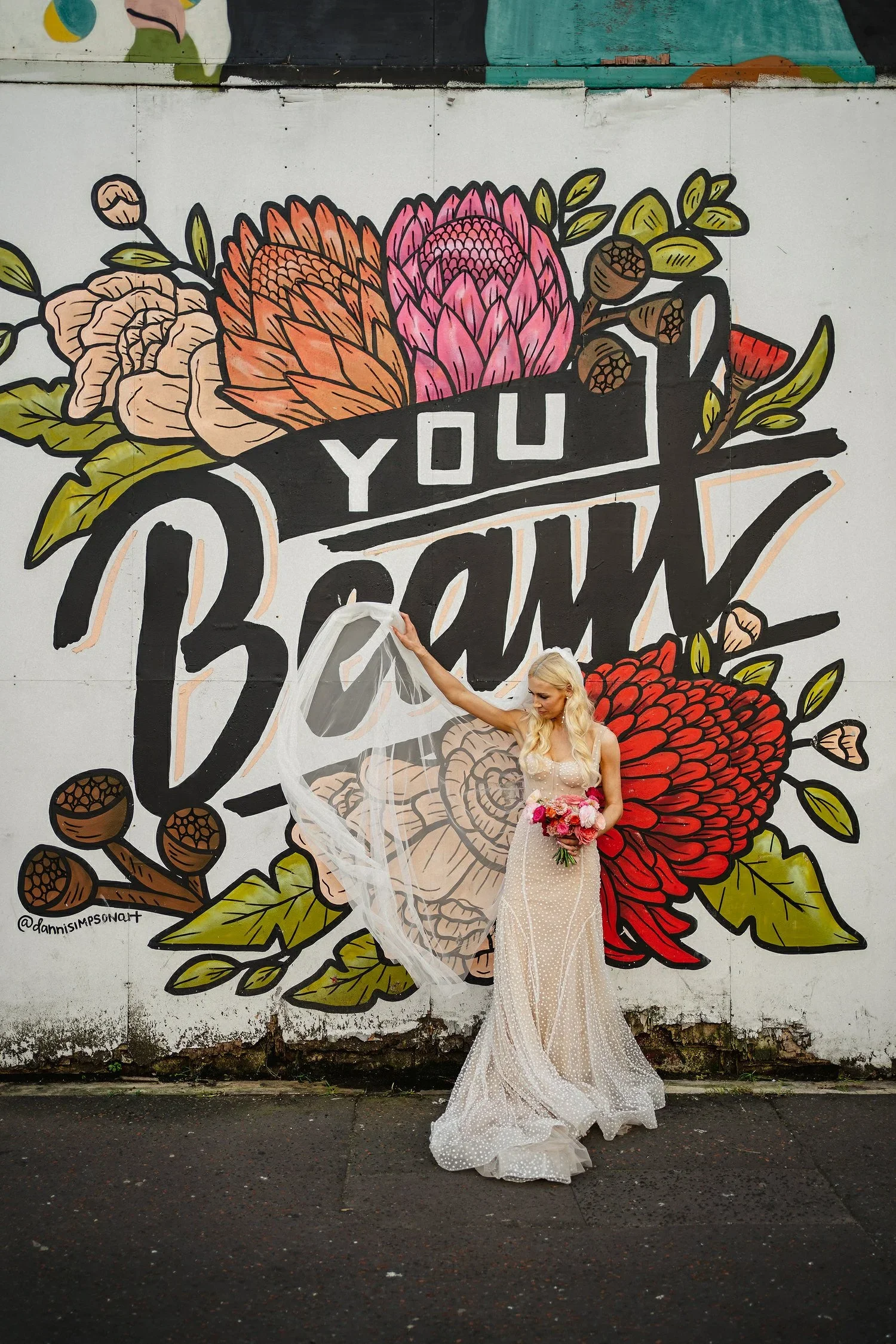 A bride poses in front of graffitti in Belfast saying you beaut.
