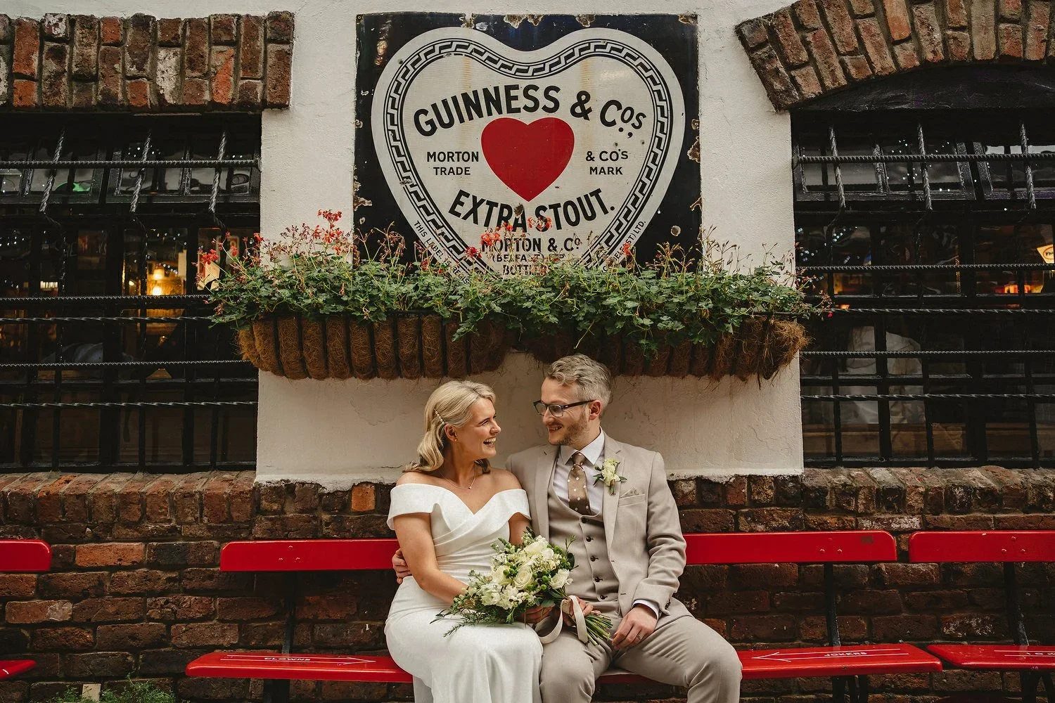 A bride and groom sit underneath a heart shaped guinness sign in Belfast Cathedral Quarter