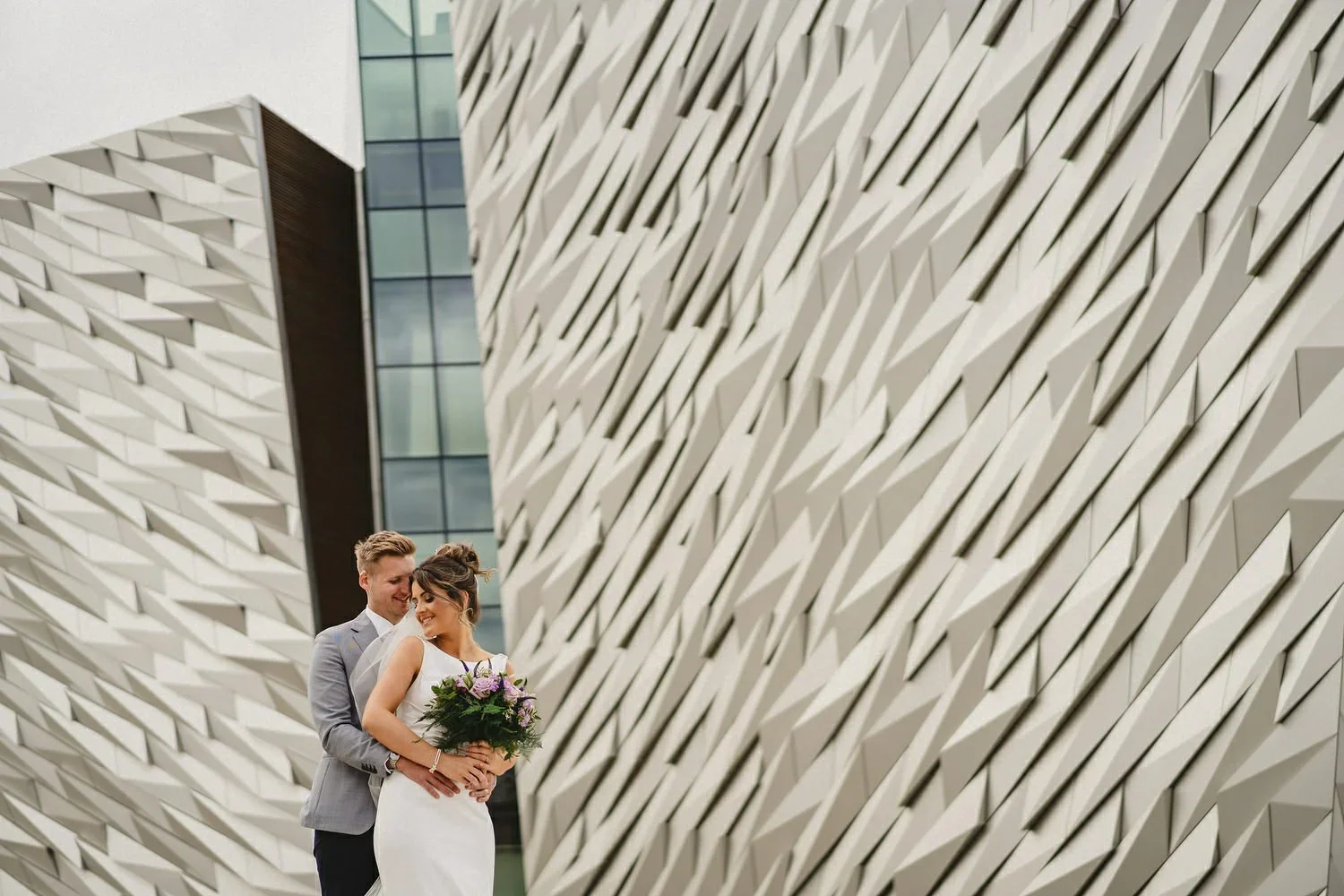 A bride and groom pose for their wedding photos outside Titanic Hotel in Belfast with the Titanic building in the background