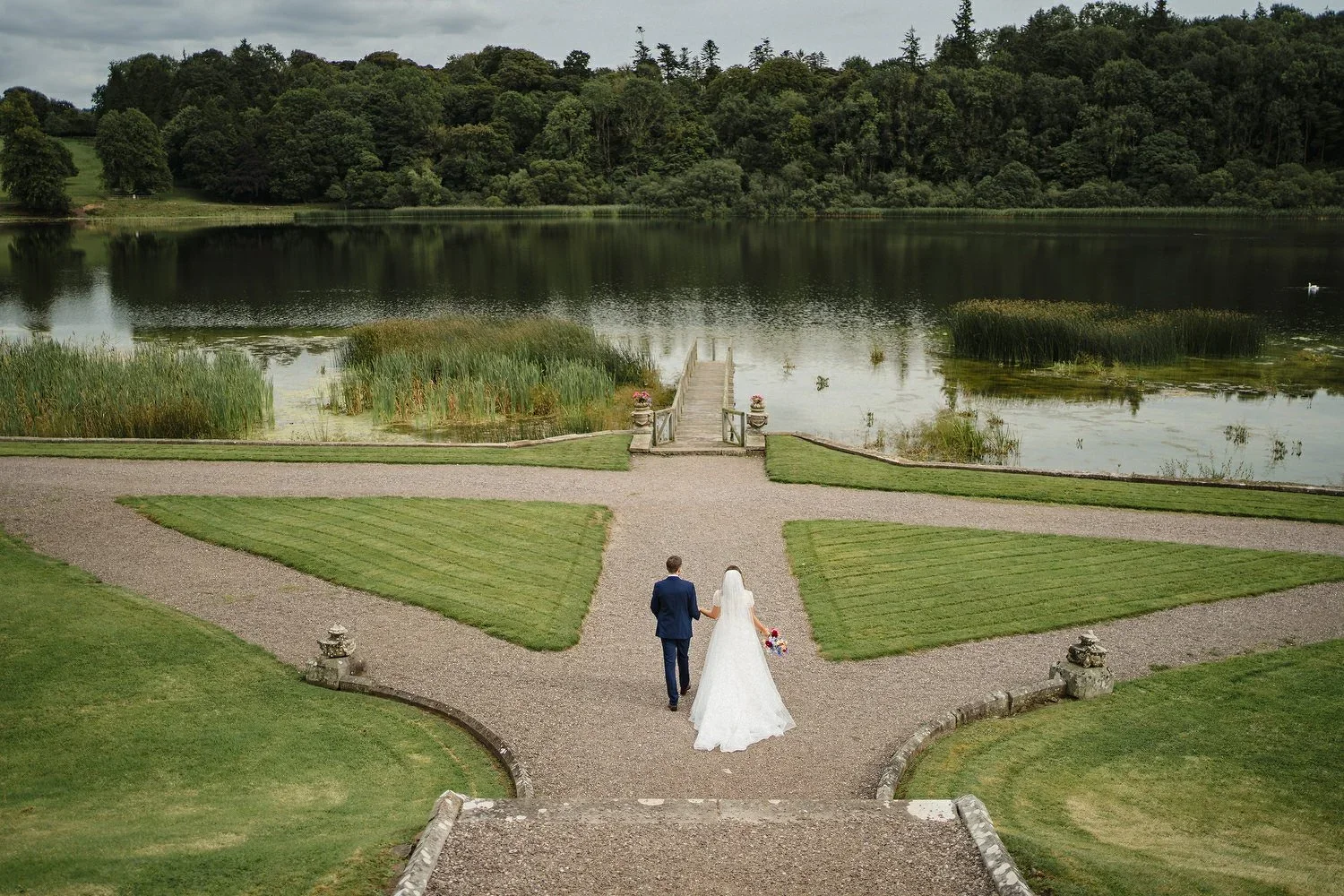 Castle Leslie lake with a bride and groom walking towards it.