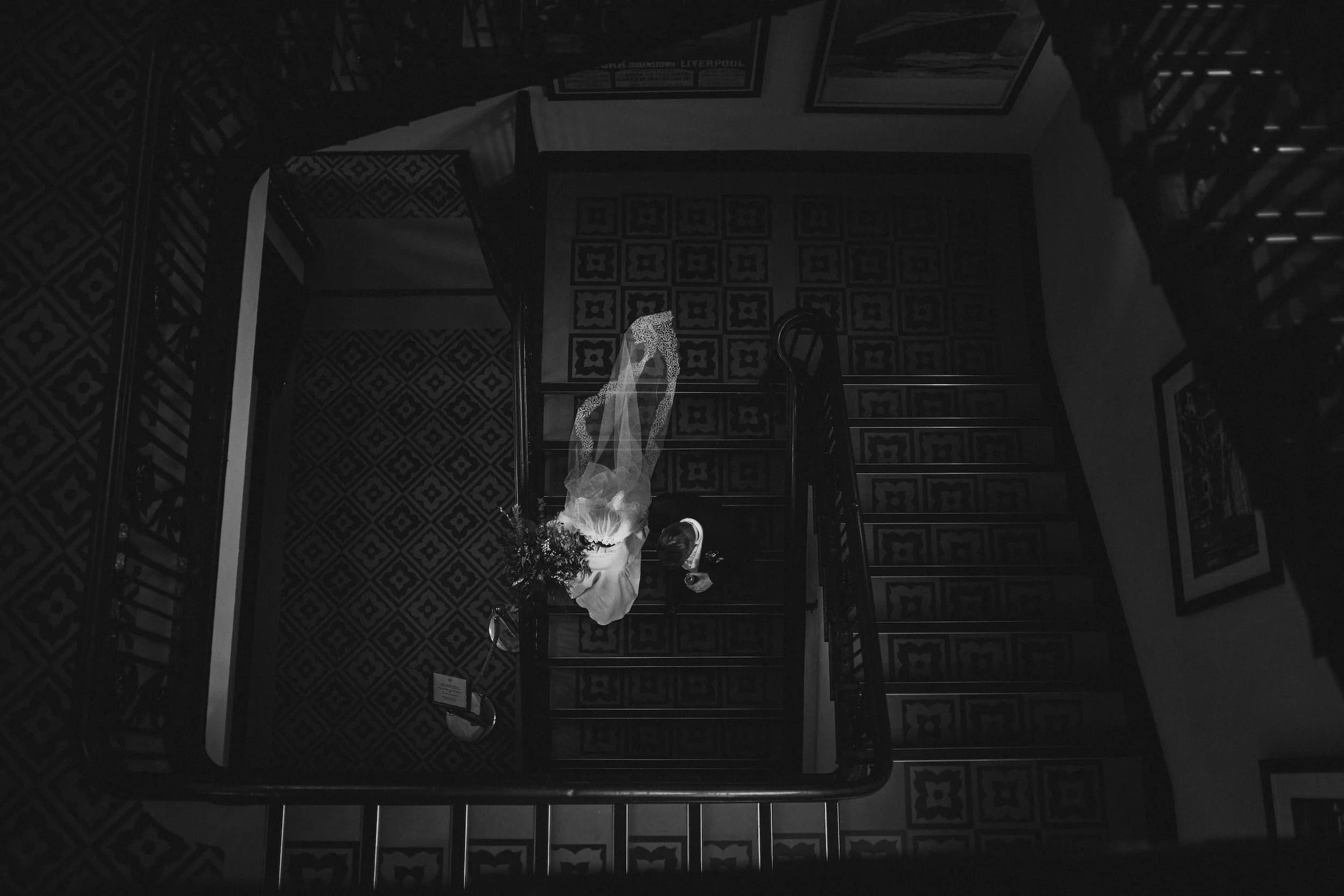 A black and white photo. A bride and groom walk down the stairs together at Titanic Hotel in Belfast.