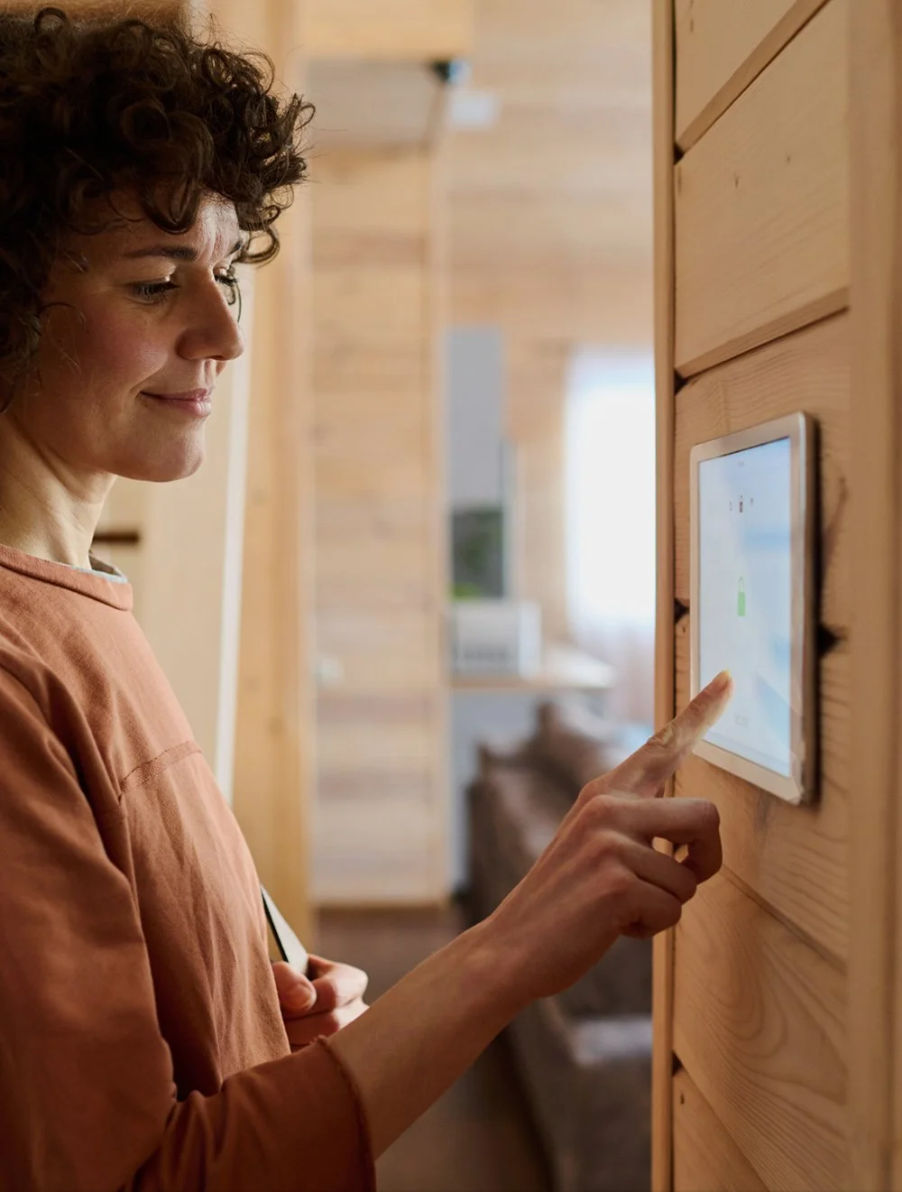 Woman interacting with a touchscreen panel mounted on a wooden wall in a cozy home interior.