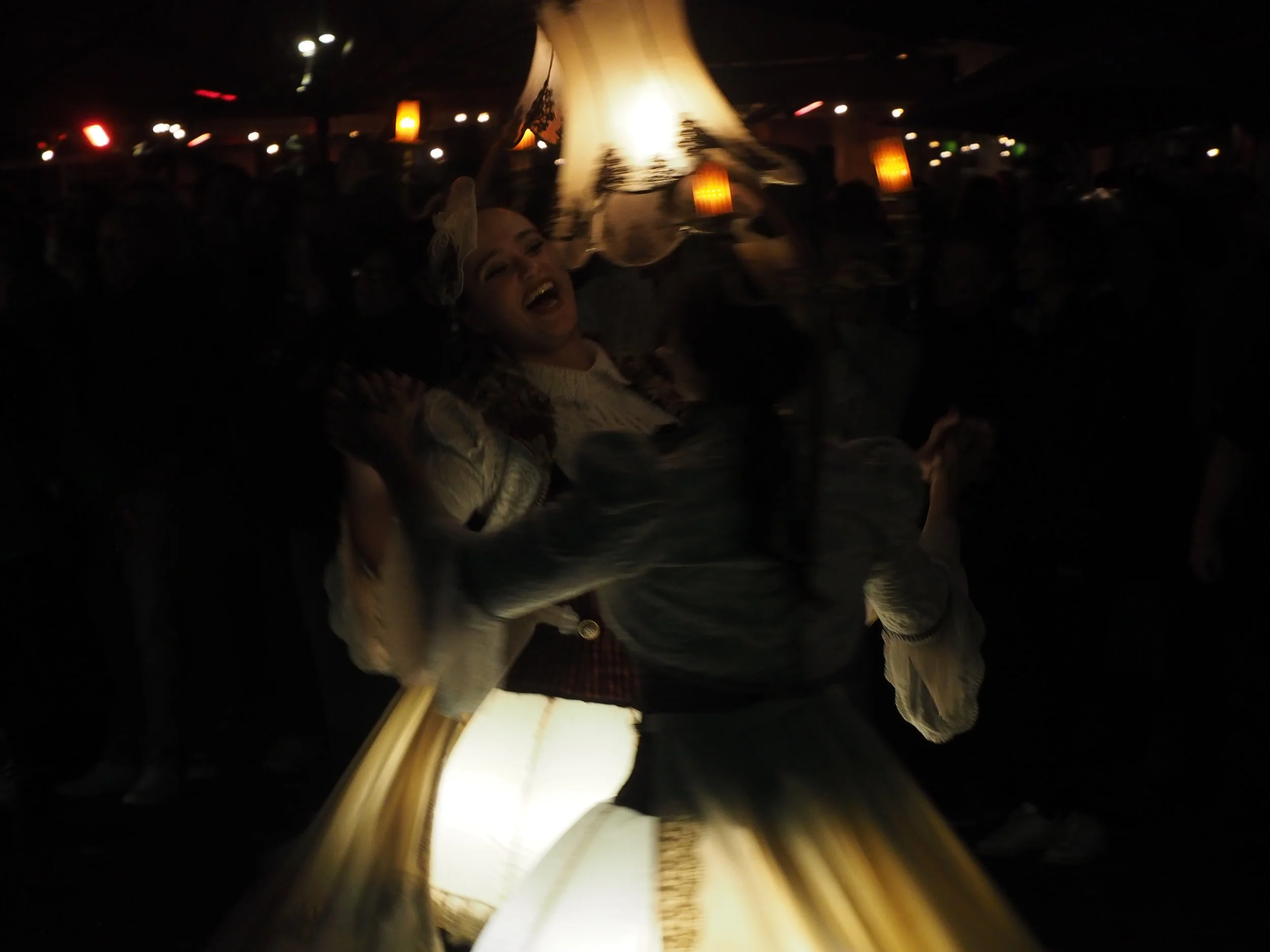 A person smiling while holding a large fish, possibly a marlin, at an indoor event with dim lighting and other people in the background.