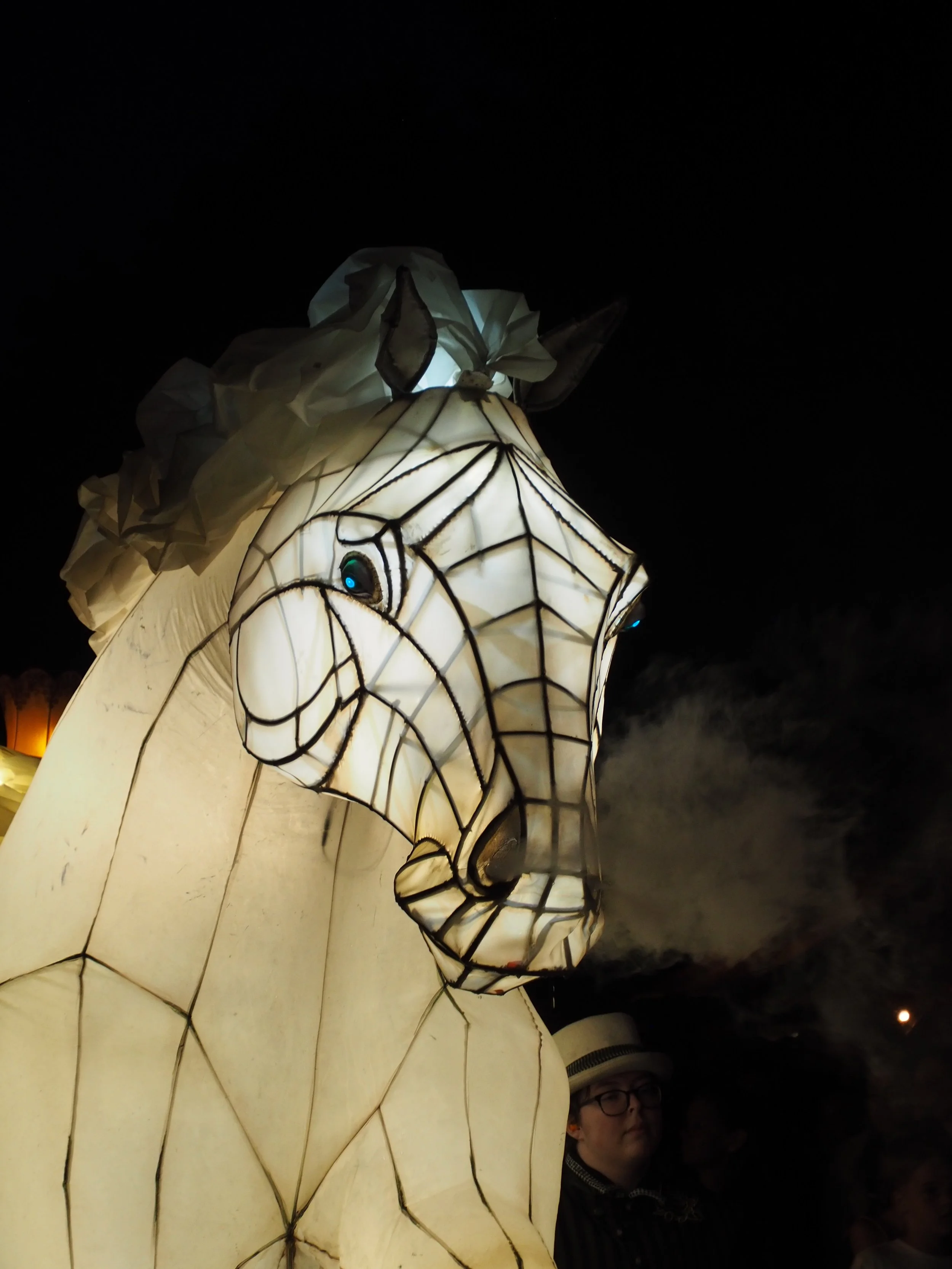 Nighttime scene with a large illuminated paper lantern shaped like a horse, with a person partially visible in the background.