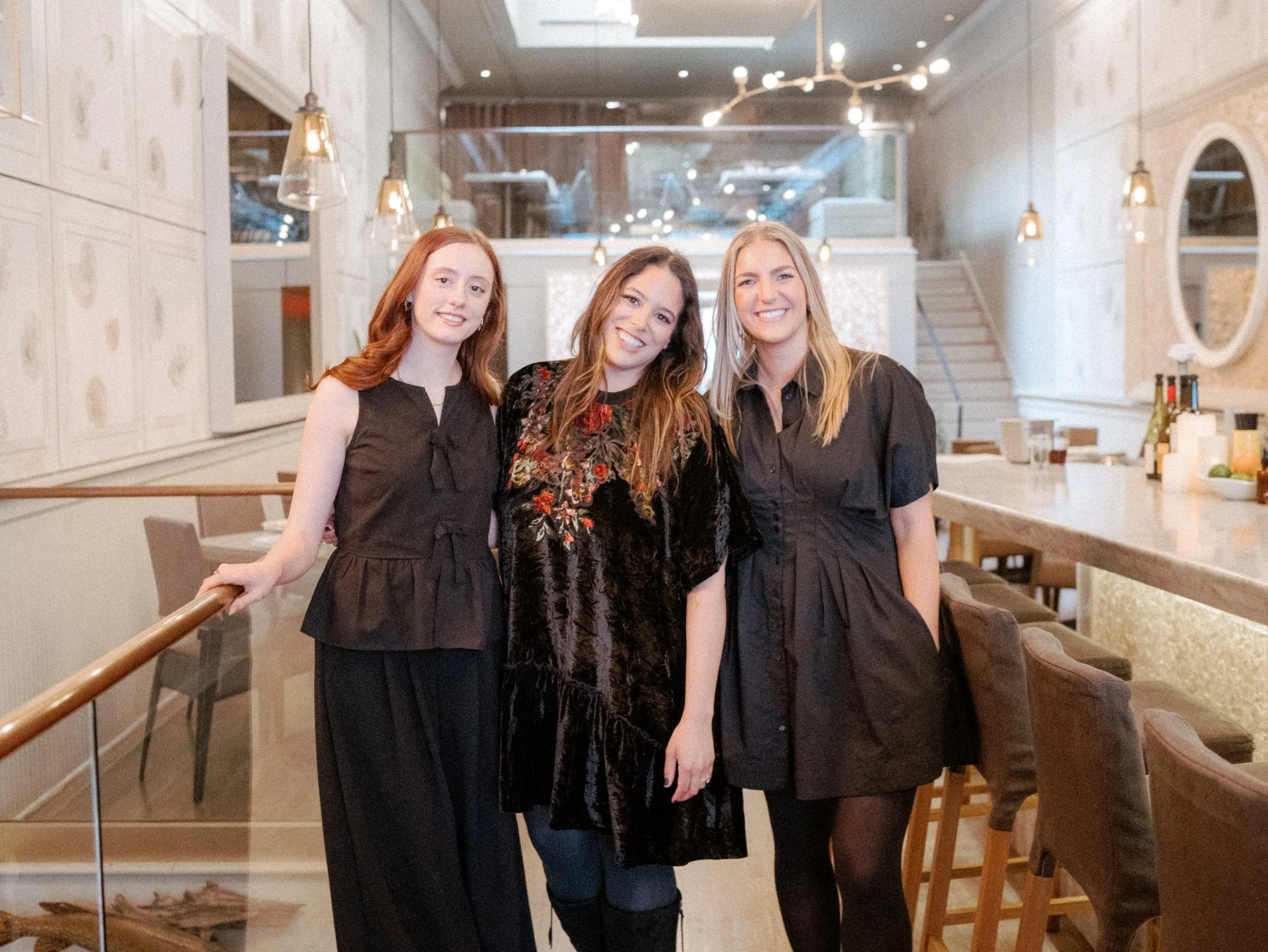 Three women standing together inside a restaurant, smiling at the camera.