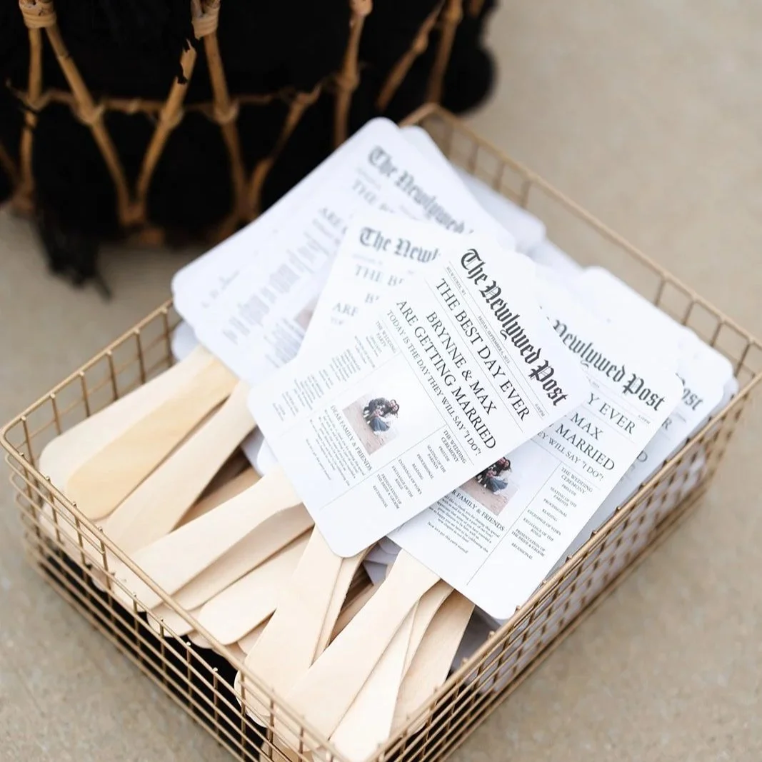 A wire basket containing wooden sticks and paper flyers for a wedding event, with the flyers announcing the couple's wedding day.