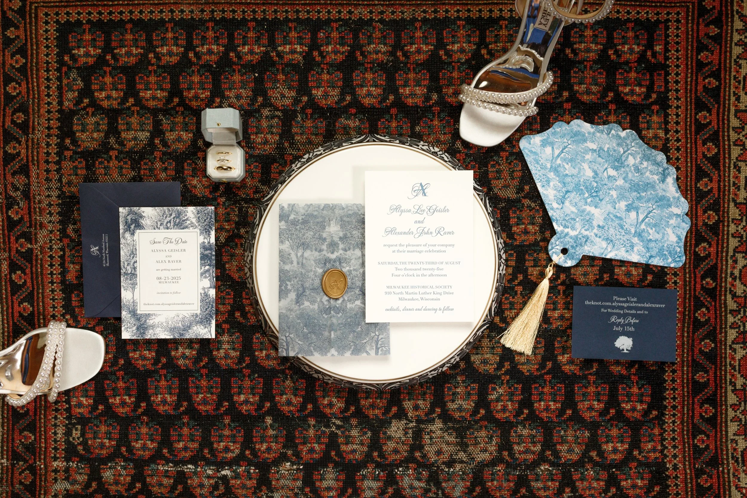Wedding invitation suite including save-the-date and invitation cards, jewelry, and a decorative hand mirror, all arranged on a patterned rug.
