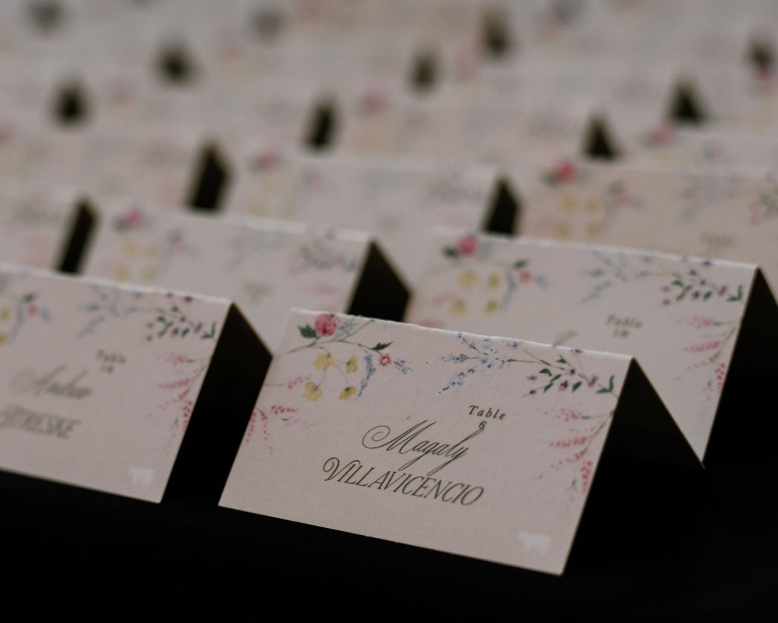Wedding table cards with floral designs and the name Magaly Villavicencio printed on them.