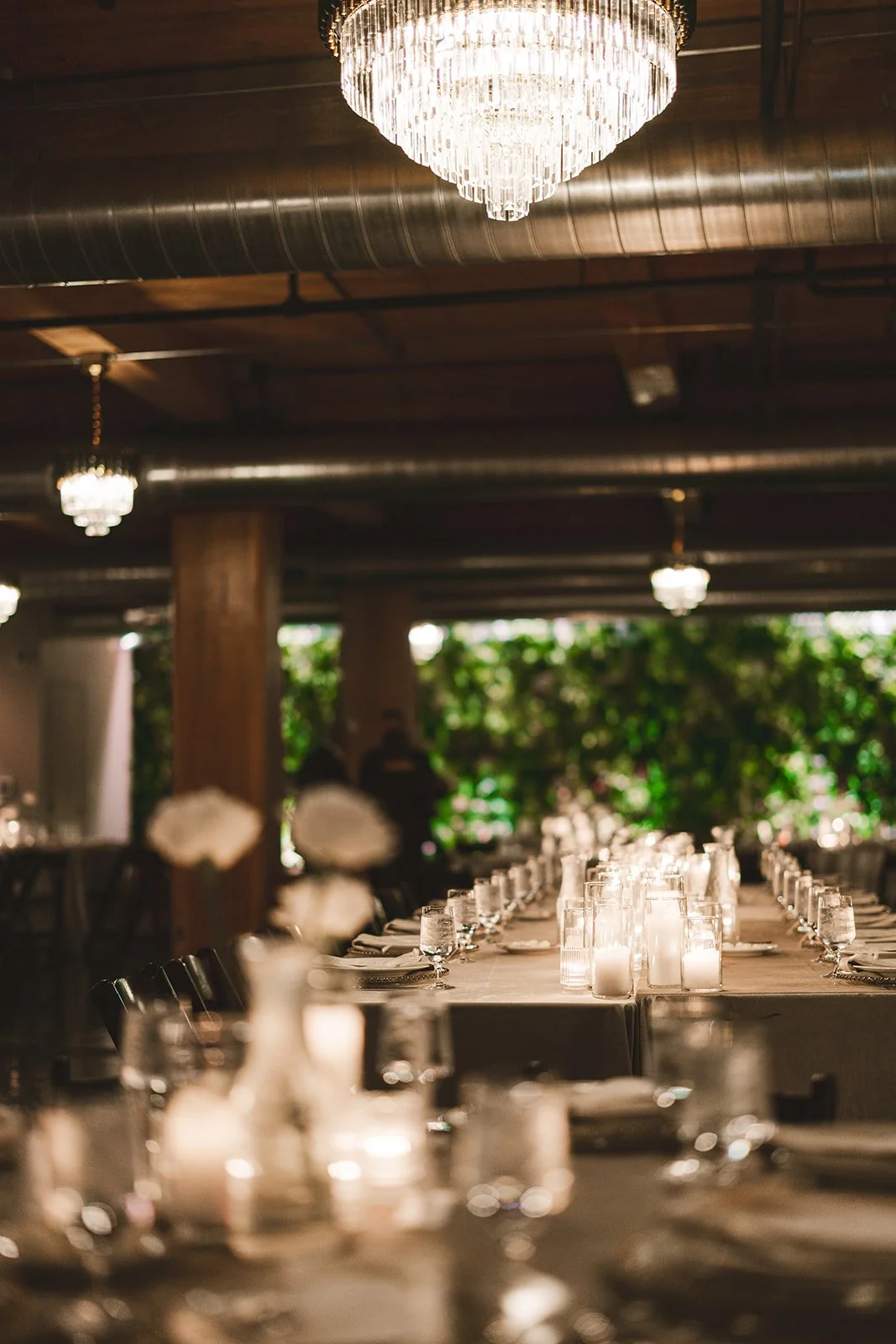 A decorated dining table set for an event with candles and glassware, under a chandelier with a wood ceiling.