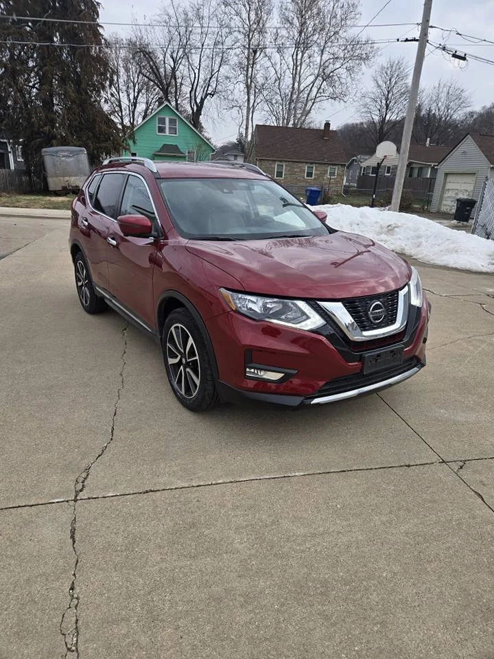 Red Nissan SUV parked on a concrete driveway in a residential neighborhood with houses, a basketball hoop, and snow in the background.