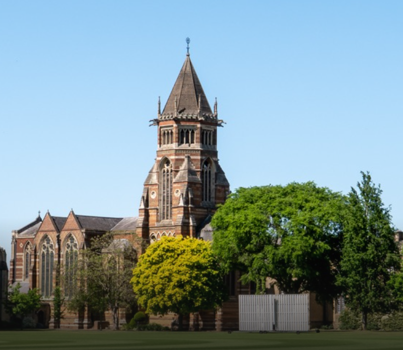 A historic church with a tall steeple surrounded by green trees in front of a clear blue sky.