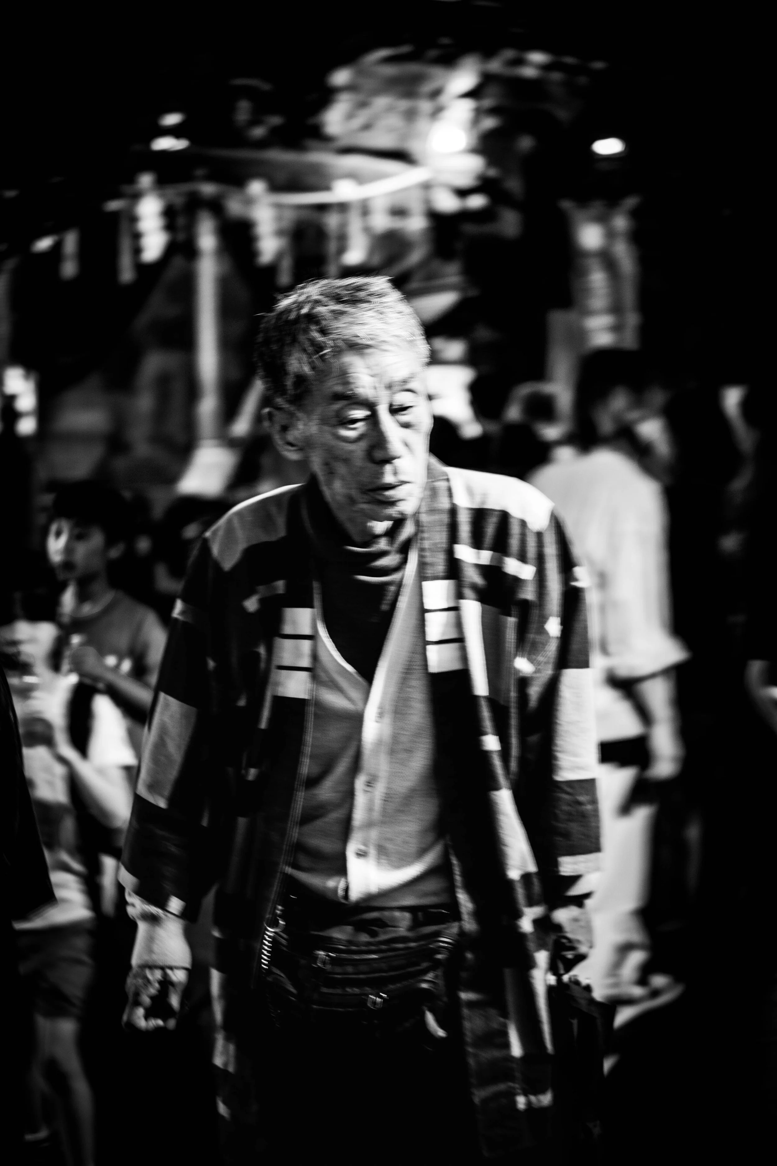 Schwarz-Weiß-Foto eines alten Mannes in einem belebten Nachtmarkt, der nachdenklich blickt.