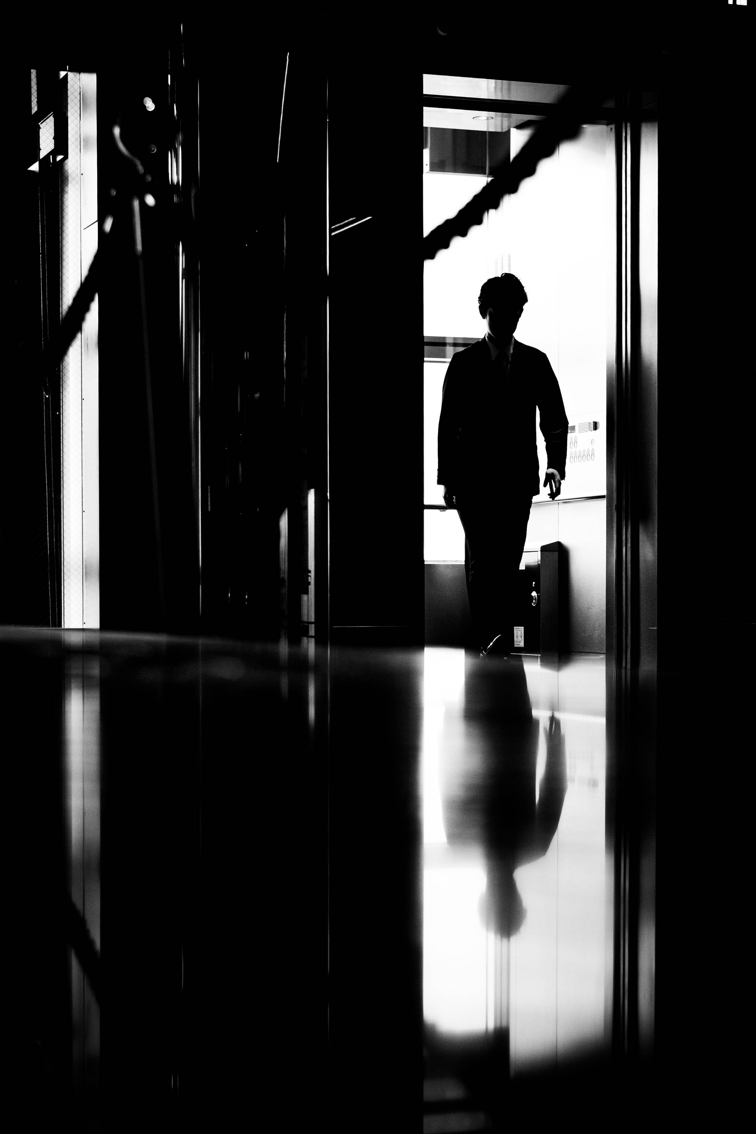 Silhouette eines Mannes in einem Aufzug oder einem modernen Gebäude, sichtbar durch ein Fenster mit natürlichem Licht, schwarze und weiße Kontraste.