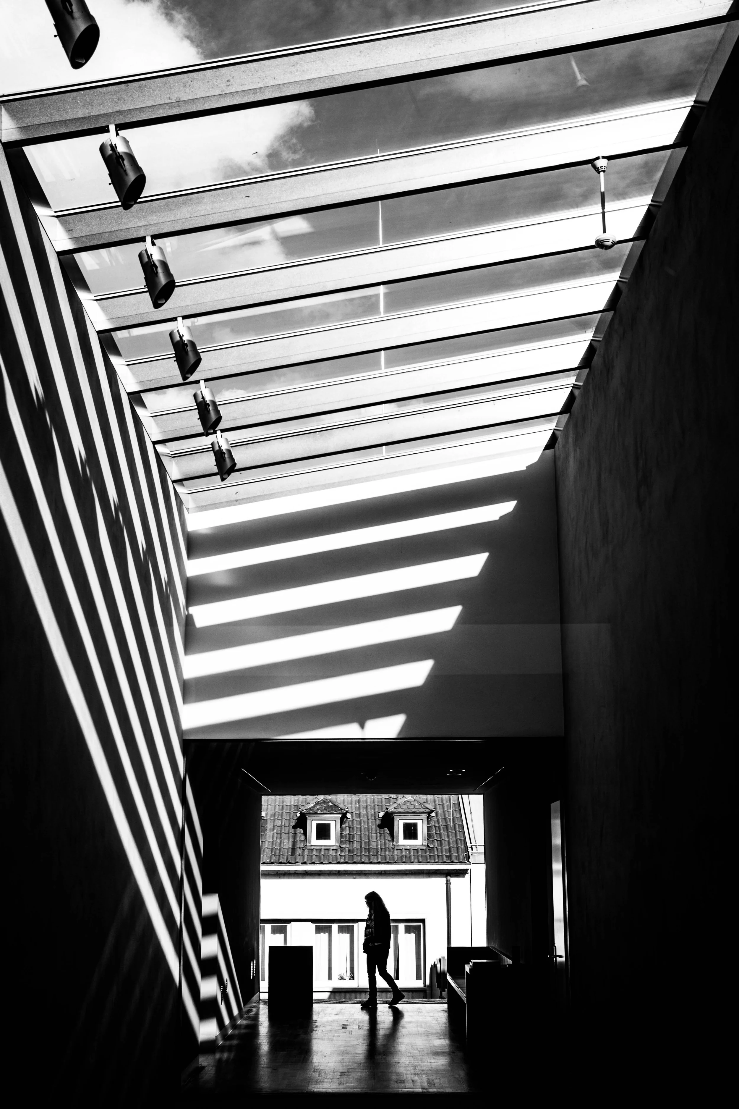 Schwarze Silhouette einer sitzenden Person in einem modernen, hellen Raum mit großen Fenstern, Sonnenschein und Schatten.