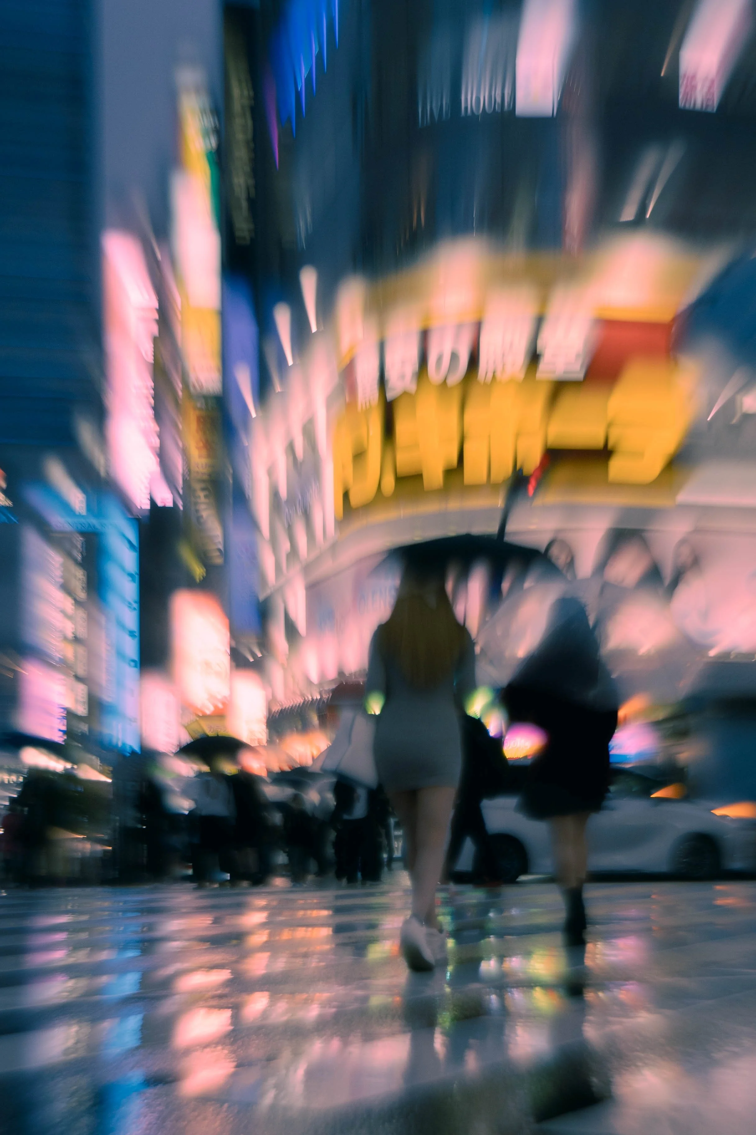Menschen mit Regenschirmen in einer belebten, nächtlichen Stadtstraße bei Regen, Neonlichter reflektieren auf nassem Bürgersteig.