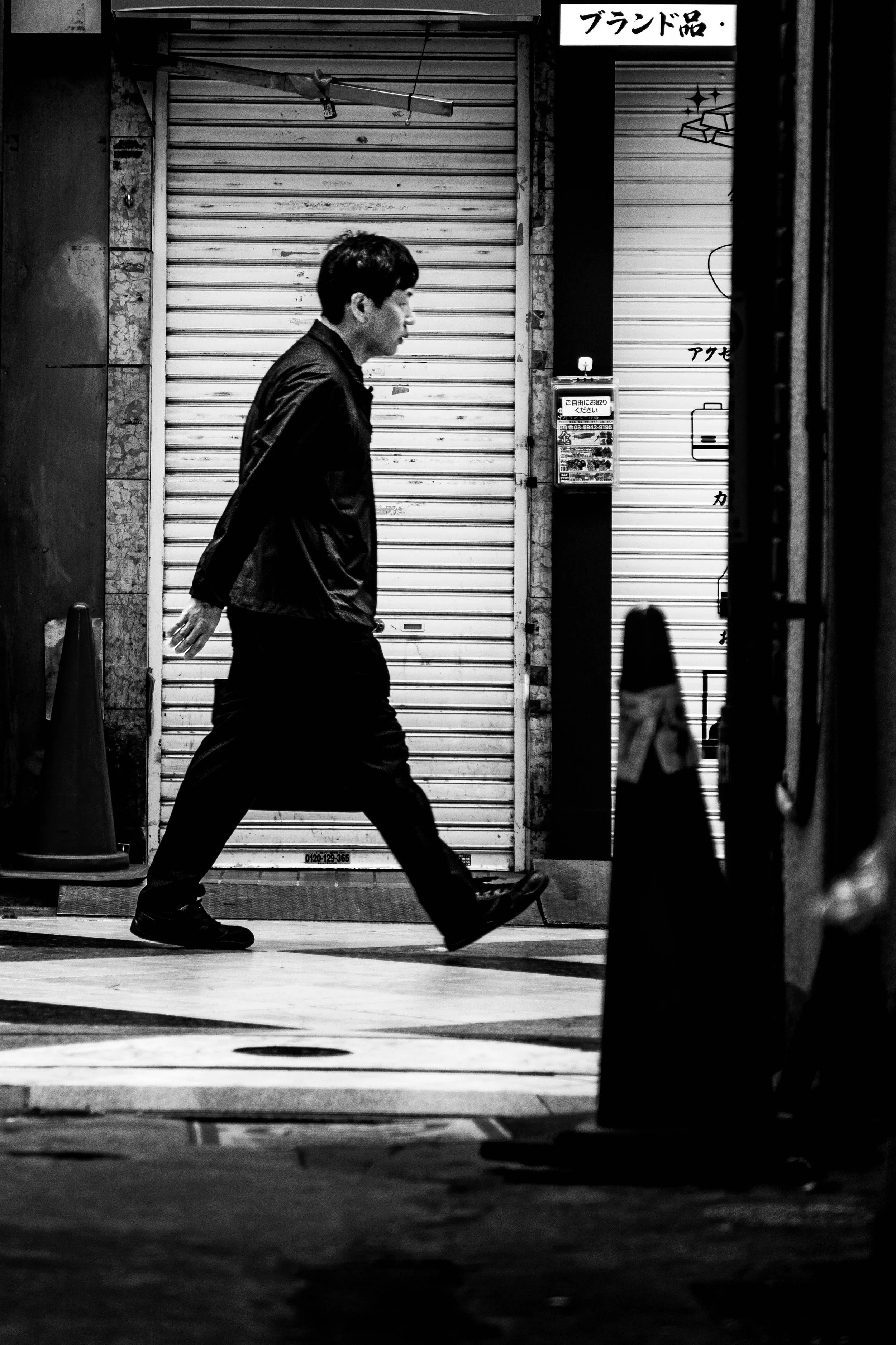 Ein Mann läuft in einer Straße in der Nacht, die im Schwarz-Weiß-Foto gezeigt wird, an einer geschlossenen Ladentür vorbei.