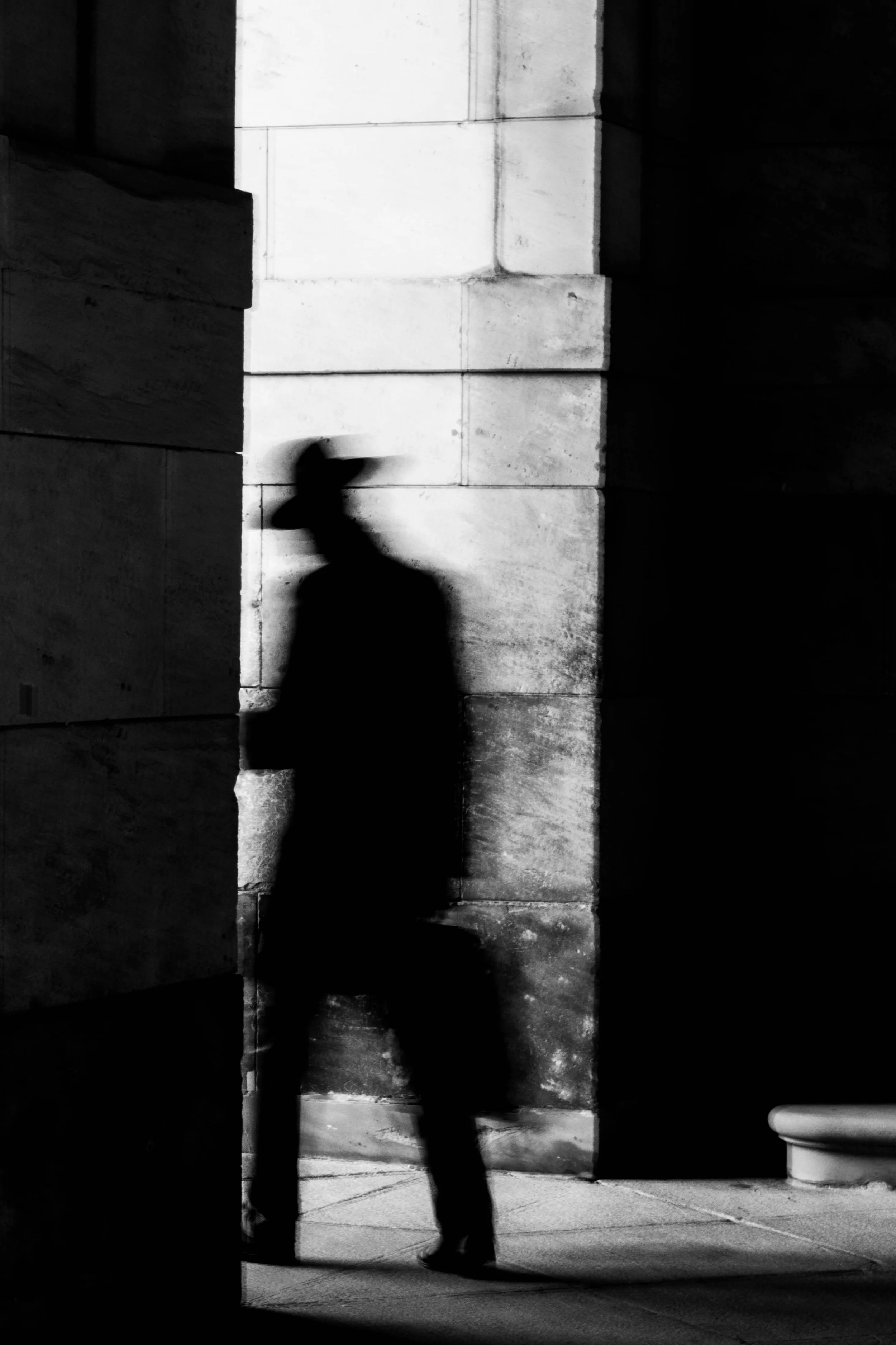 Silhouettenhafte Figur eines Mannes mit Hut, der im Schatten an einer Wand lehnt.