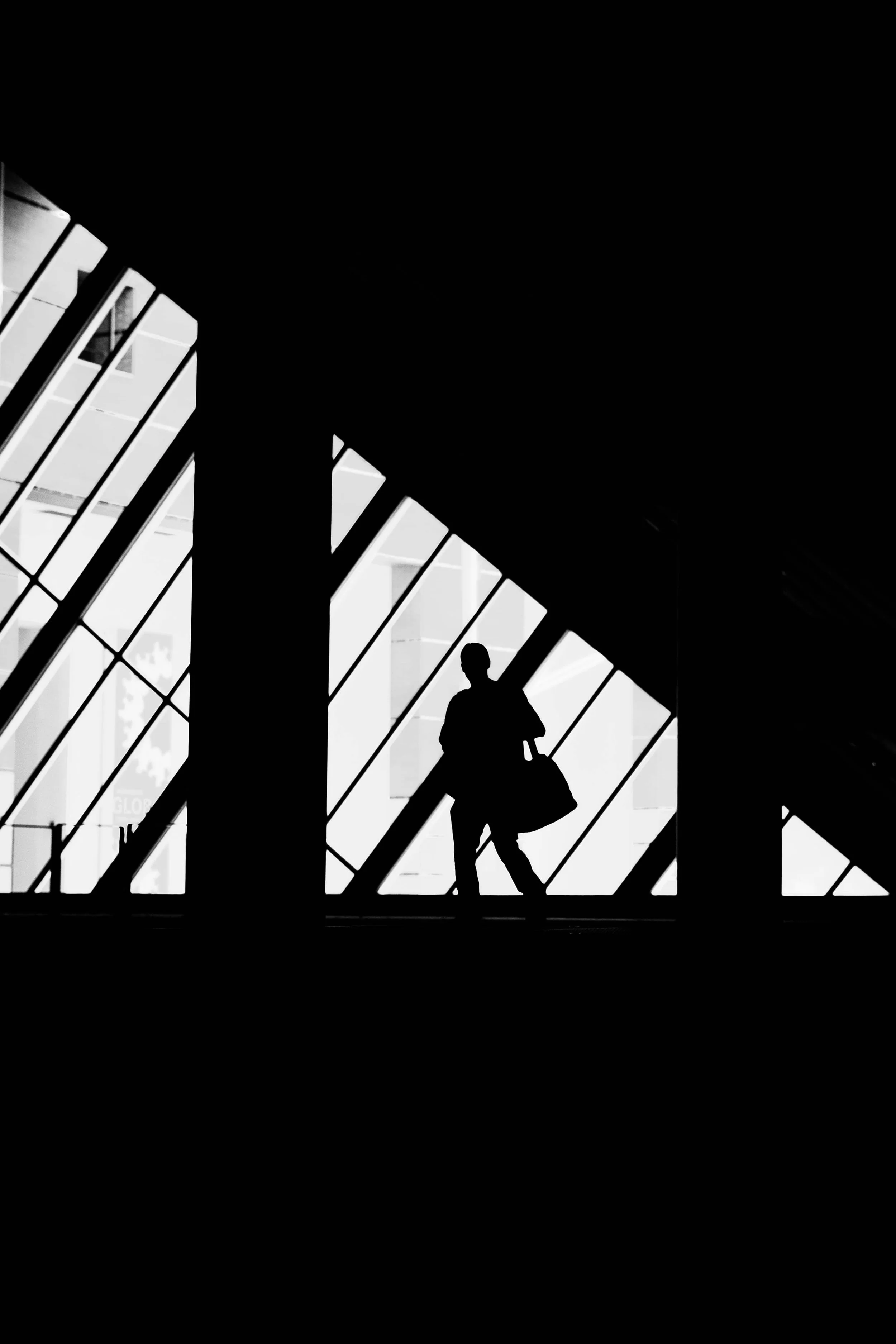 Silhouette einer Person mit Reisetasche in einem modernen Gebäude mit großen Glasfenstern.