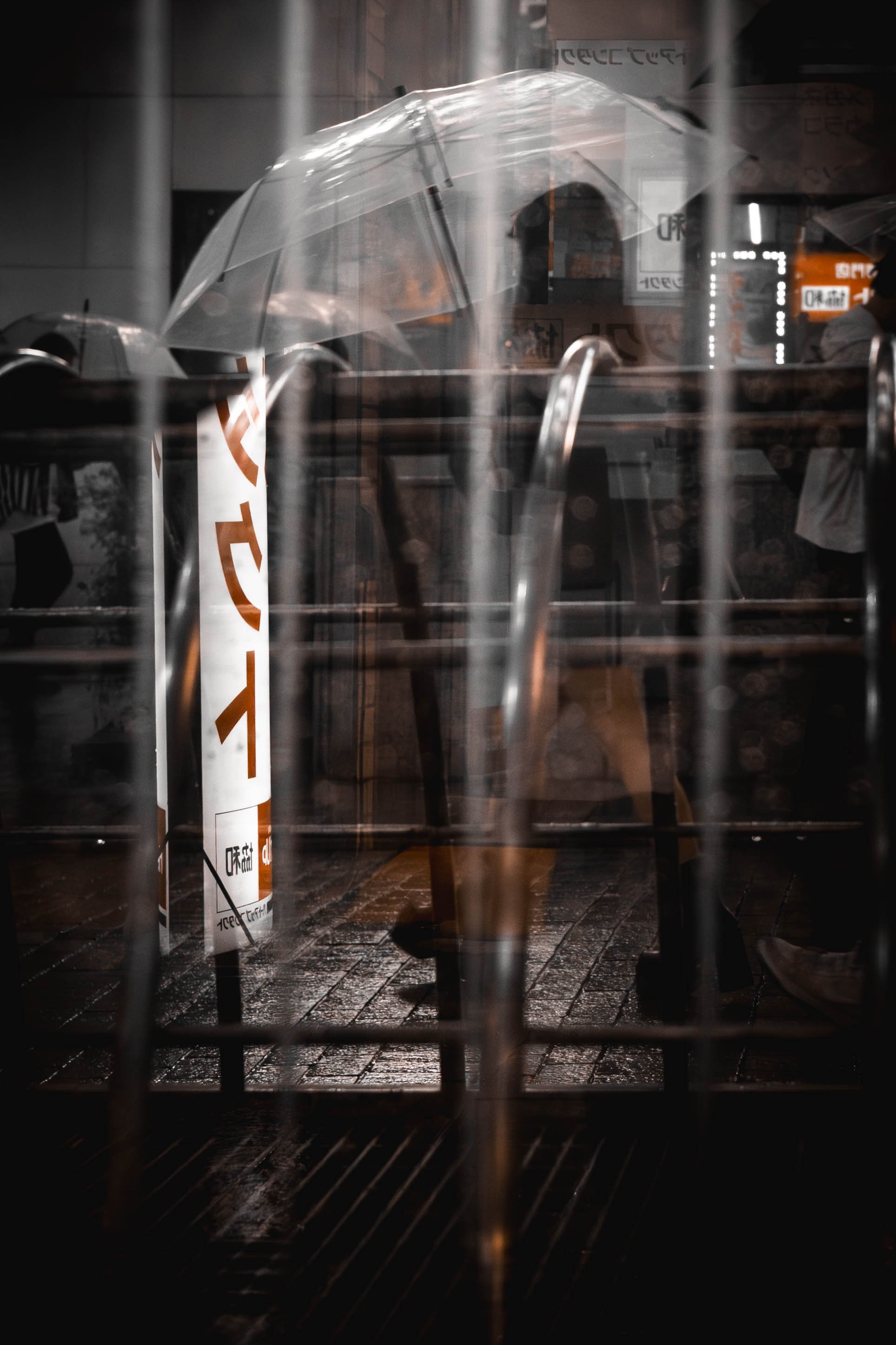 Leeres Café oder Restaurant mit einem transparenten Regenschirm, der auf einem Tisch steht, durch die Scheibe betrachtet, bei regnerischem Wetter.