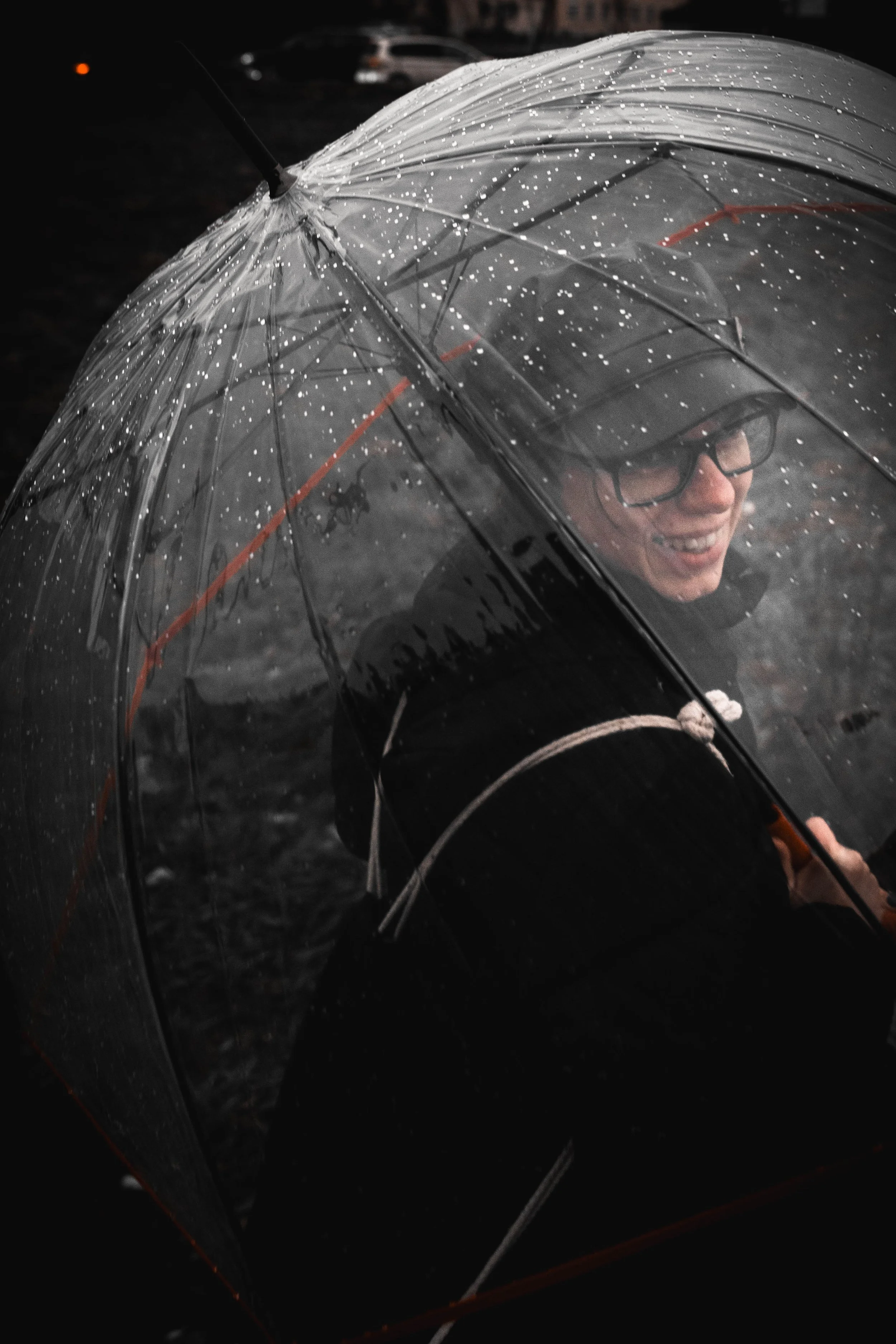 Lächelnder Mann mit Brille unter einem transparenten Regenschirm im Regen