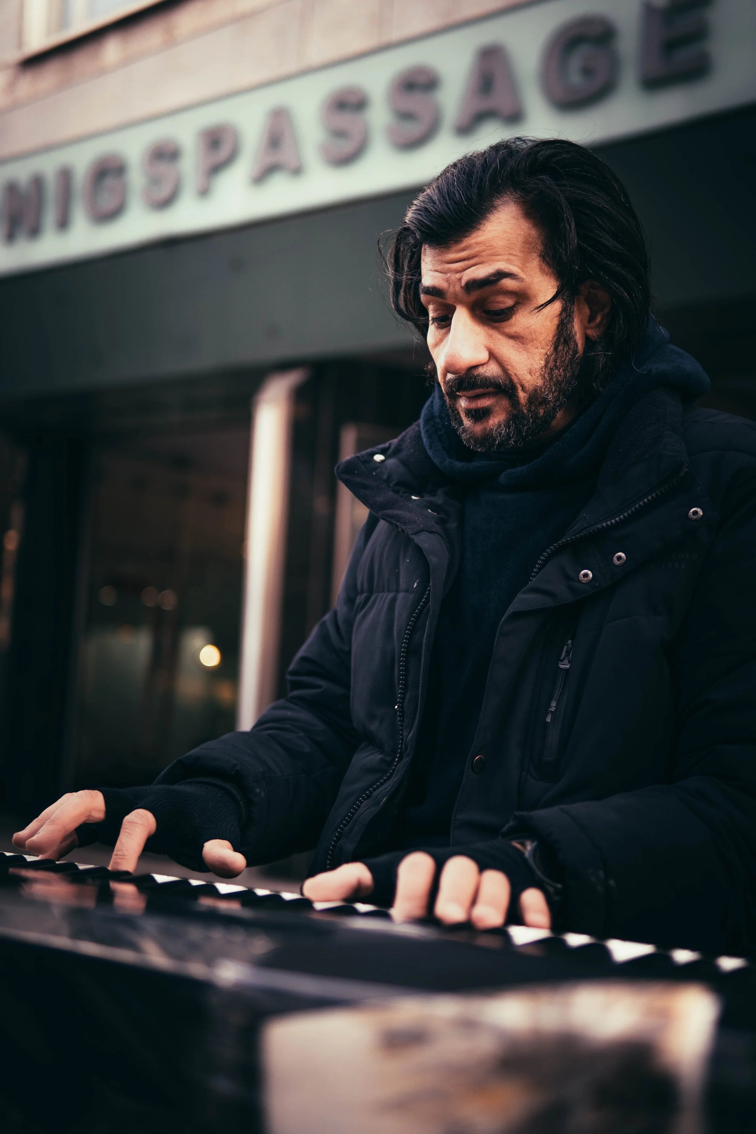 Mann spielt auf einem Keyboard im Freien vor einem Gebäude mit einem Schild, auf dem 'NIGSS PASSAGE' steht.