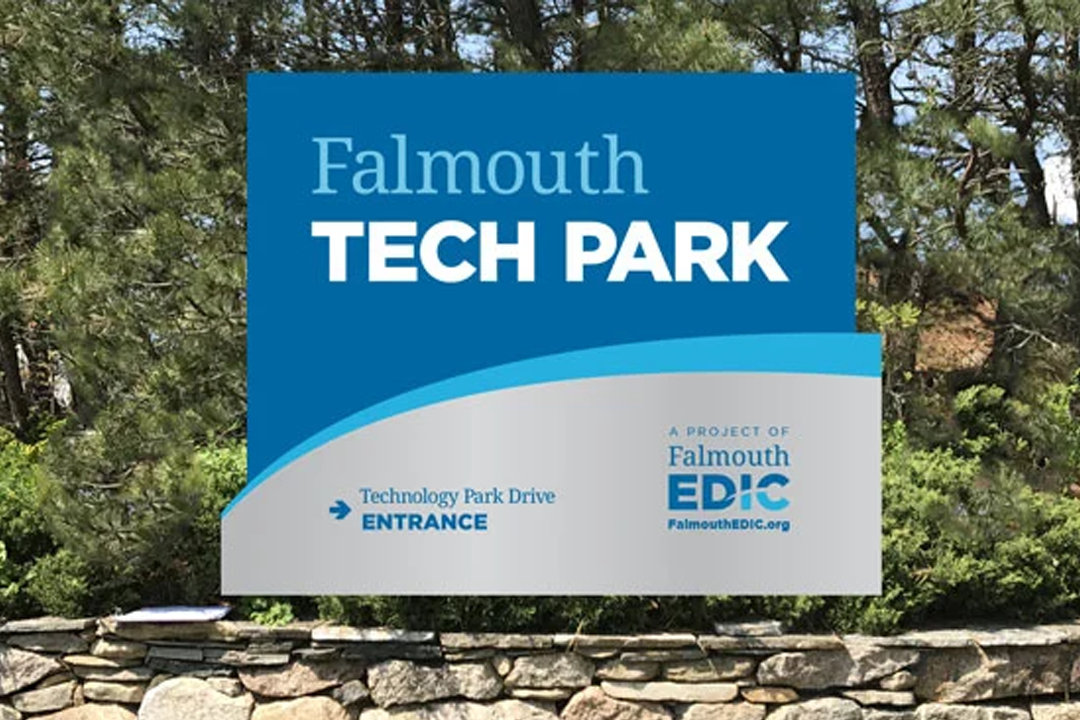 Sign for Falmouth Tech Park with trees and stone wall in background.
