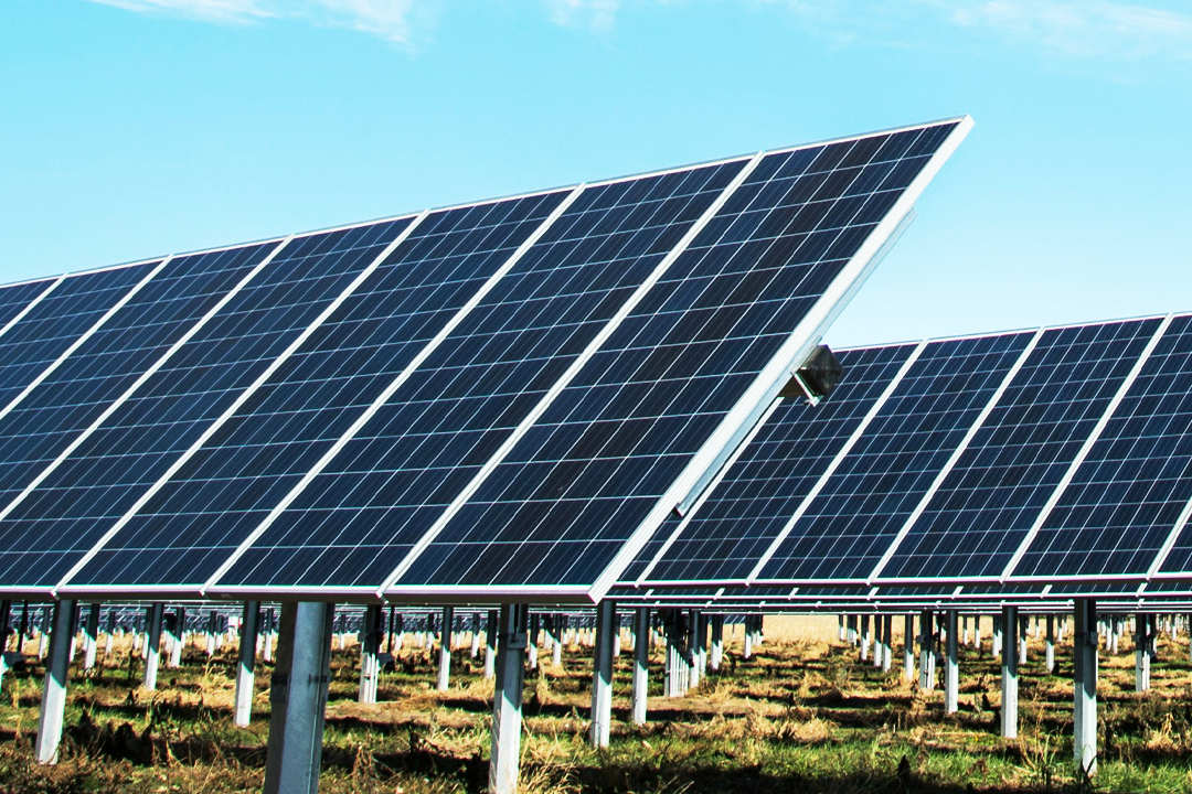 A solar farm with multiple black solar panels installed on metal supports under a blue sky.