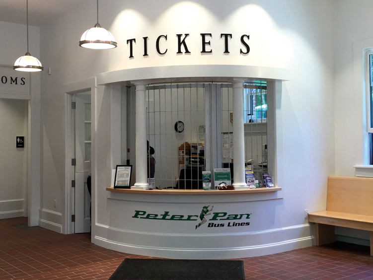 Bus ticket counter at Peter Pan Bus Lines with a sign reading 'Tickets' above, desks inside, and brochures on the counter.