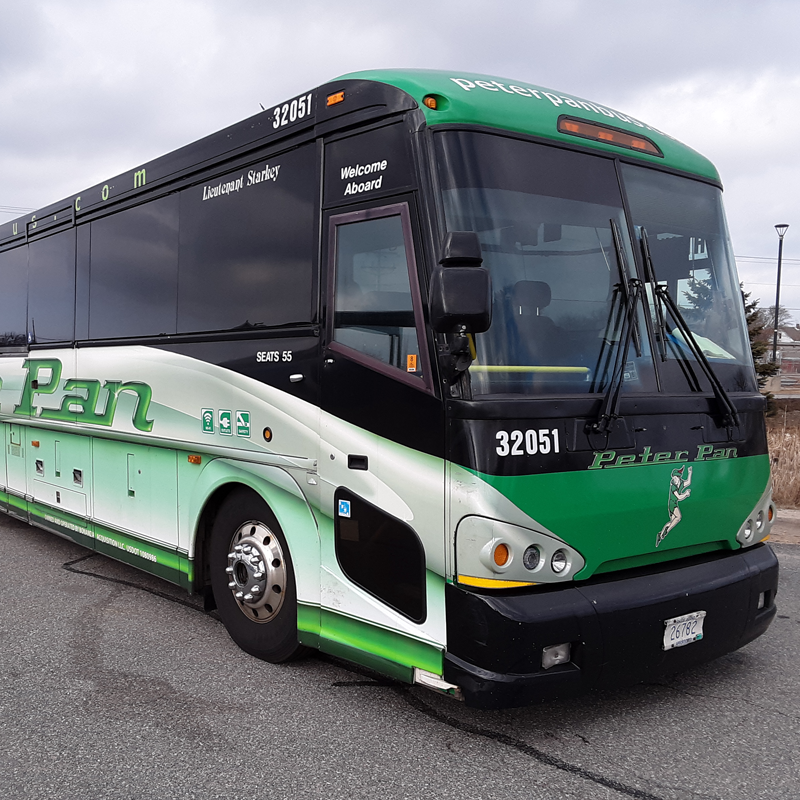 A Peter Pan bus with green, black, and white colors parked on a road with a cloudy sky in the background.