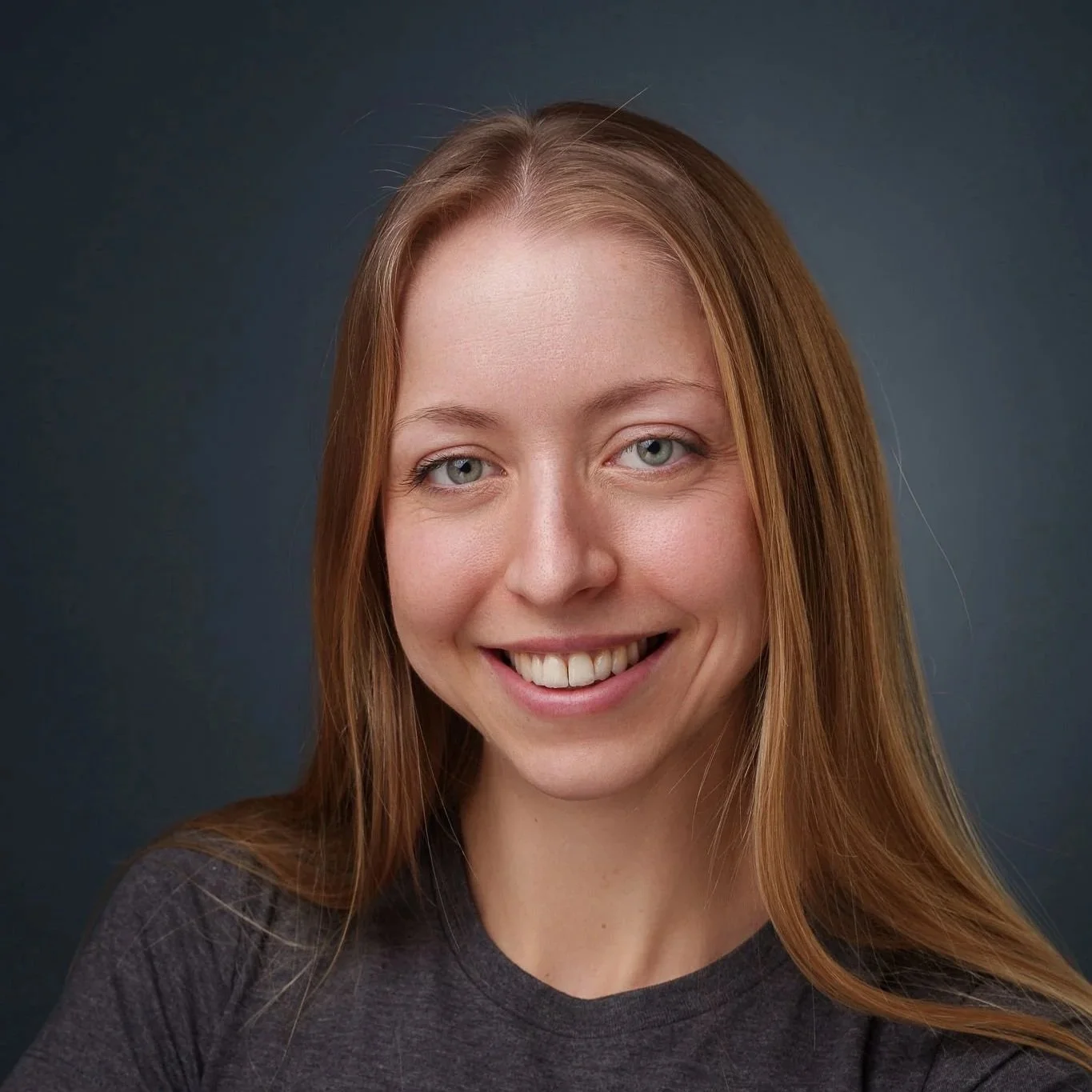 Nahaufnahme eines lächelnden jungen Mädchens mit roten Haaren und blauen Augen vor dunklem grauem Hintergrund.