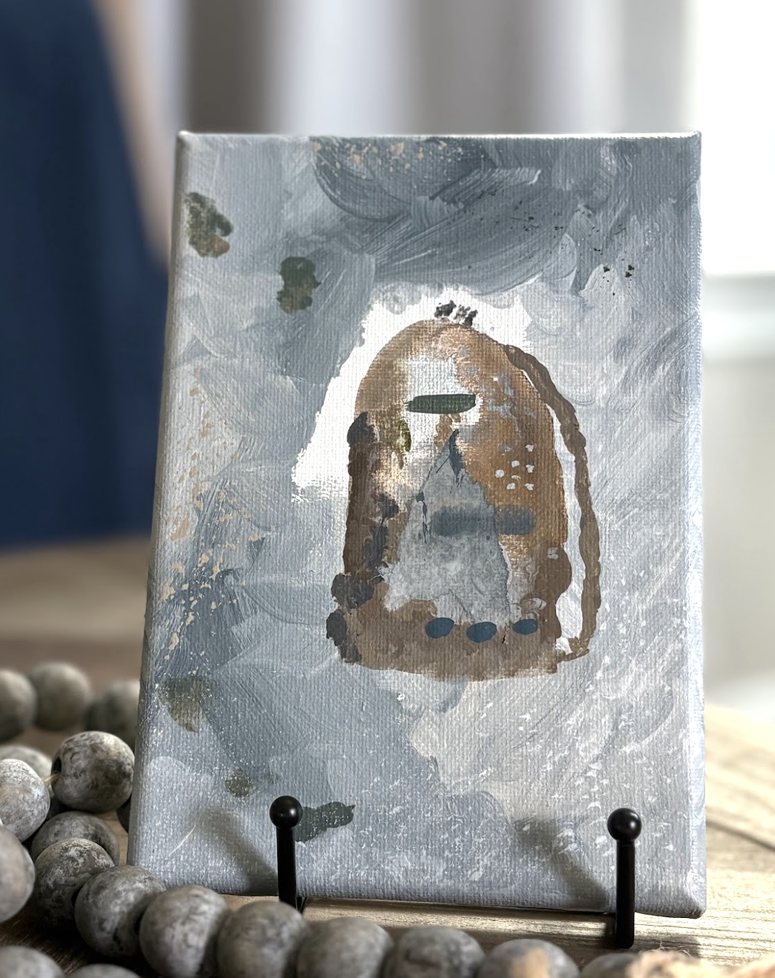 abstract painting with a figure of a backpack or book bag on an easel surrounded by wooden rustic beads